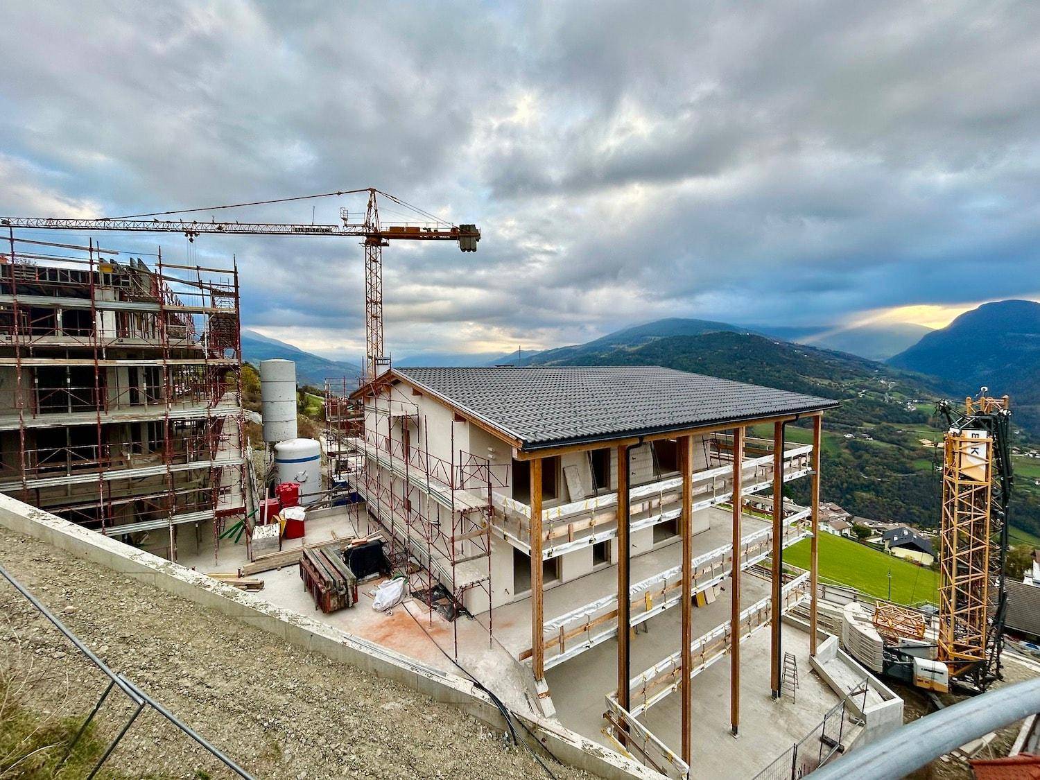Baustelle mit mehreren Gebäuden im Bau und Kränen vor einer malerischen Bergkulisse.