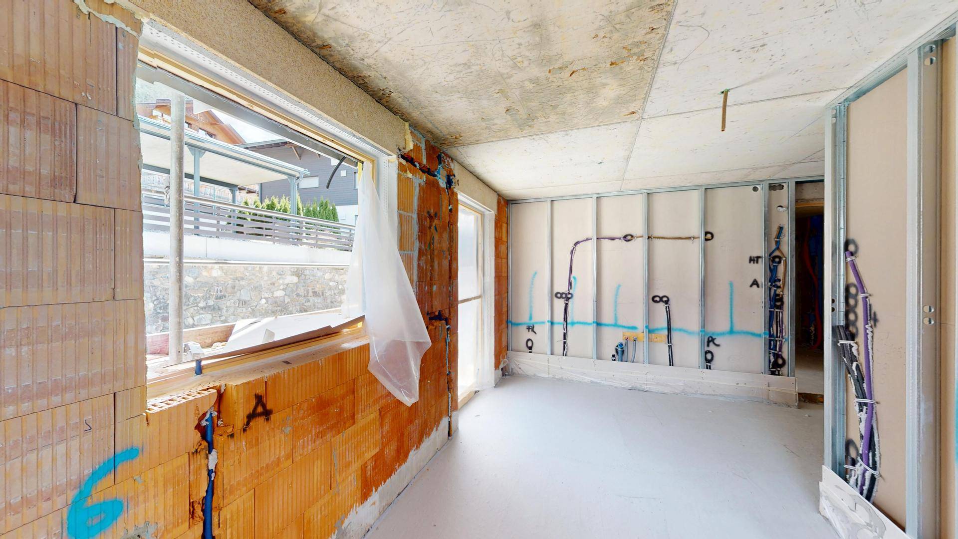 Rohbauzimmer mit Ziegelwänden, Fenstern und vorbereiteten Leitungen für Installationen.