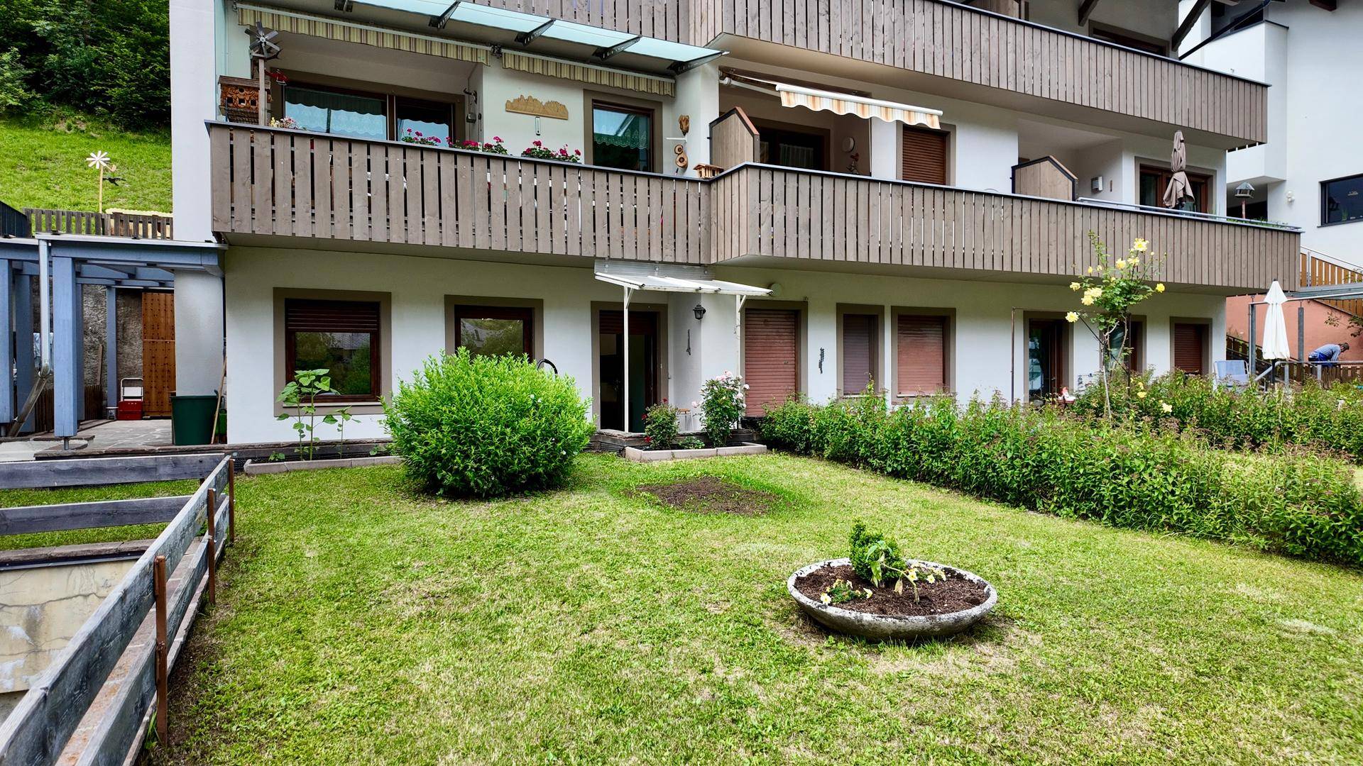 Mehrere Balkone mit Holzgeländern und ein gepflegter Gartenbereich mit Rasenfläche am Gebäude.