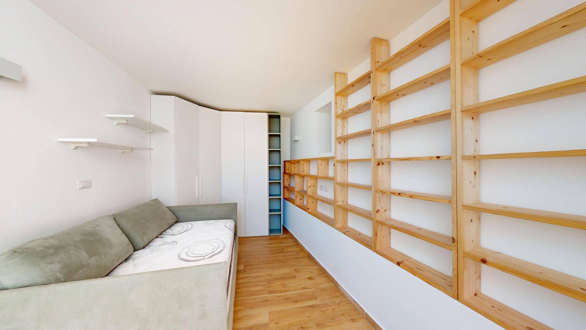 Gemütliches Zimmer mit Schlafsofa, weißem Kleiderschrank und maßgefertigten Holzregalen an der Wand.