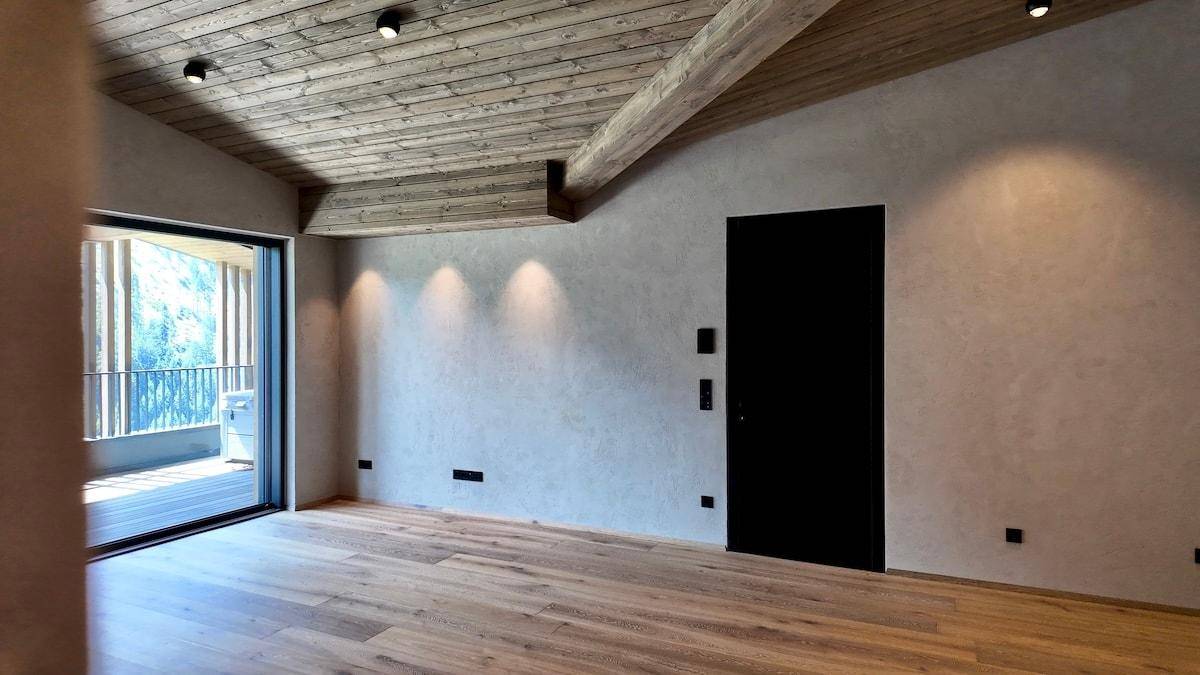 Geräumiges Wohnzimmer mit Holzboden, Holzbalkendecke und Zugang zu einem Balkon.