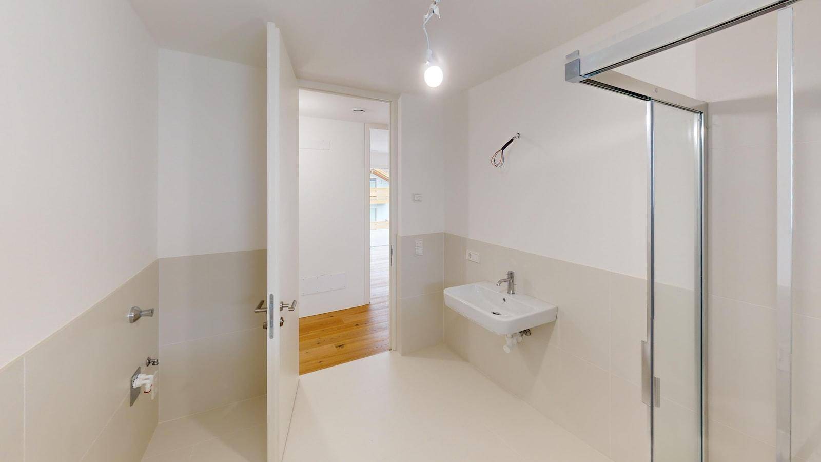 Modernes Badezimmer mit Duschbereich und Waschbecken, hell gefliest und mit Zugang zum Flur.