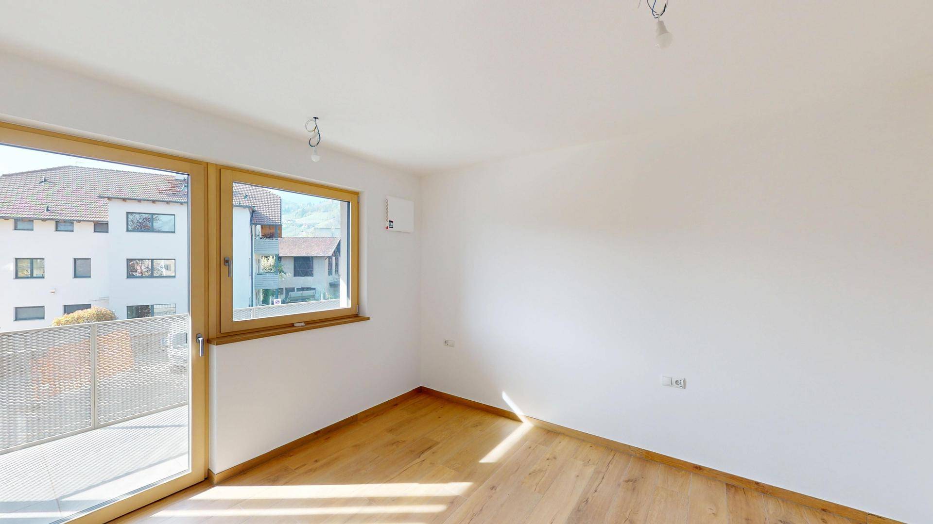 Helles Zimmer mit Holzboden, großem Fenster und direktem Zugang zu einem Balkon.