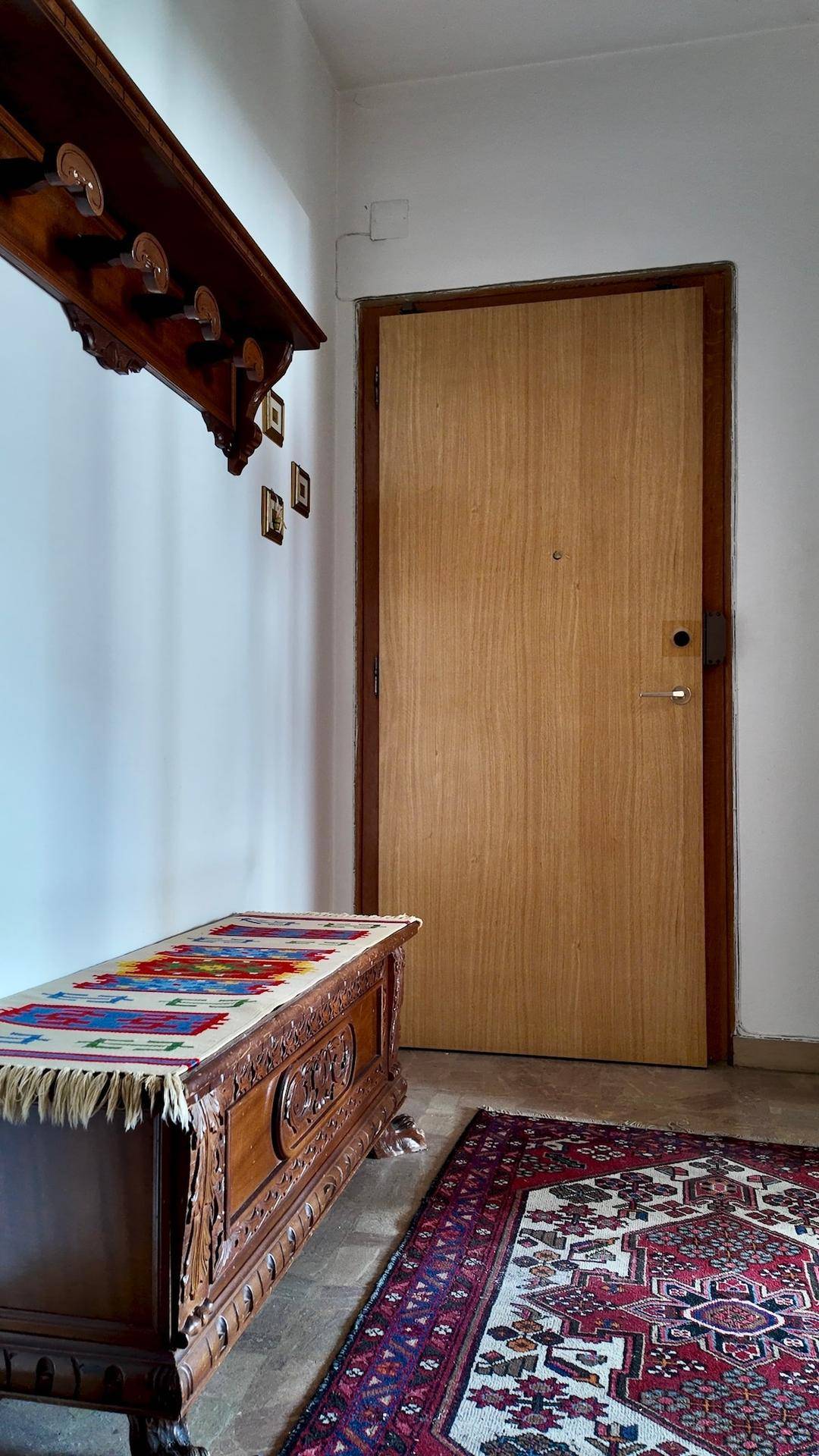 Heller Eingangsbereich mit Holztür, Teppich und einer verzierten Holzkommode.