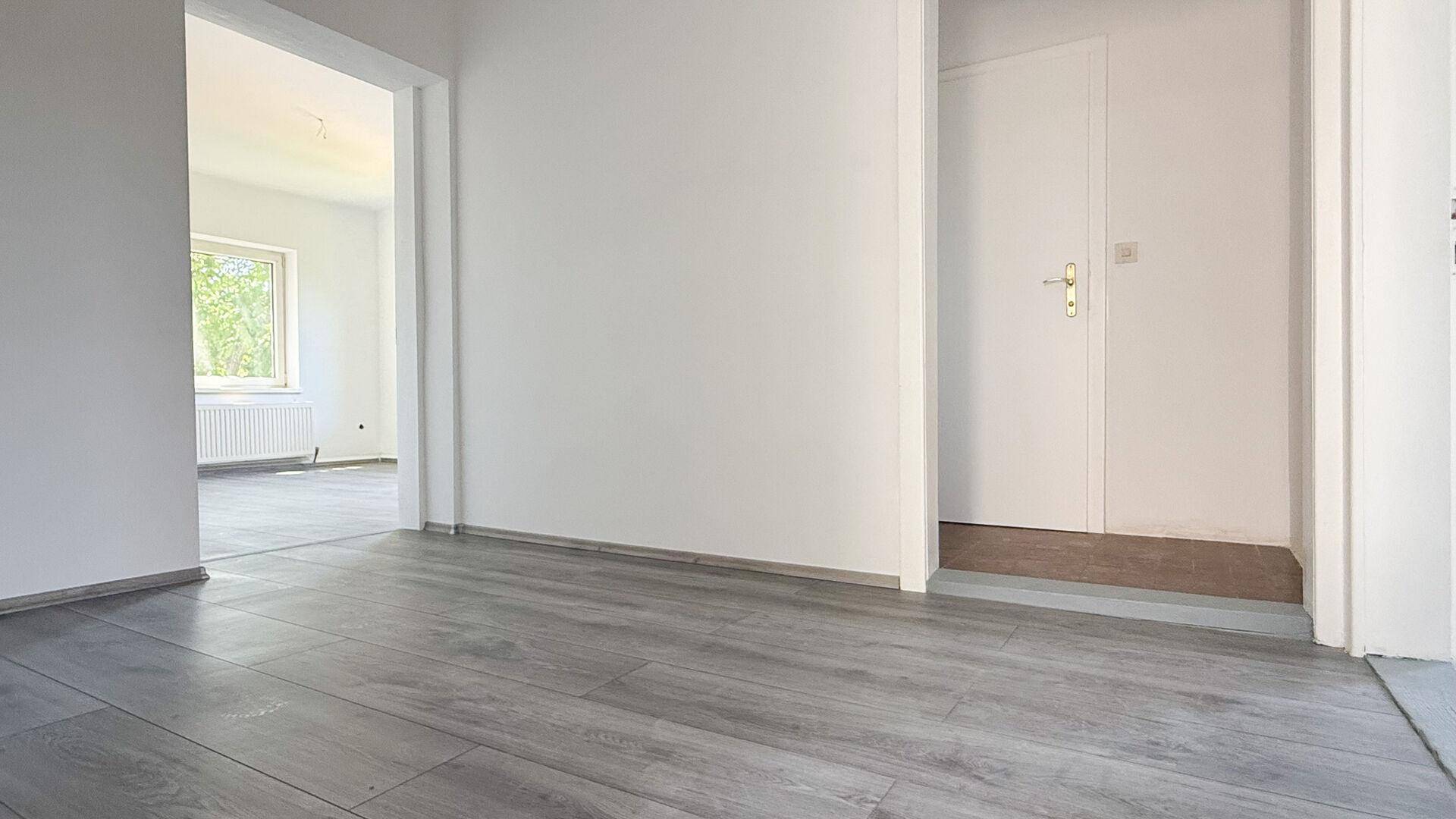 Heller Flur mit grauem Laminatboden und Zugang zu weiteren Räumen sowie einer weißen Tür.