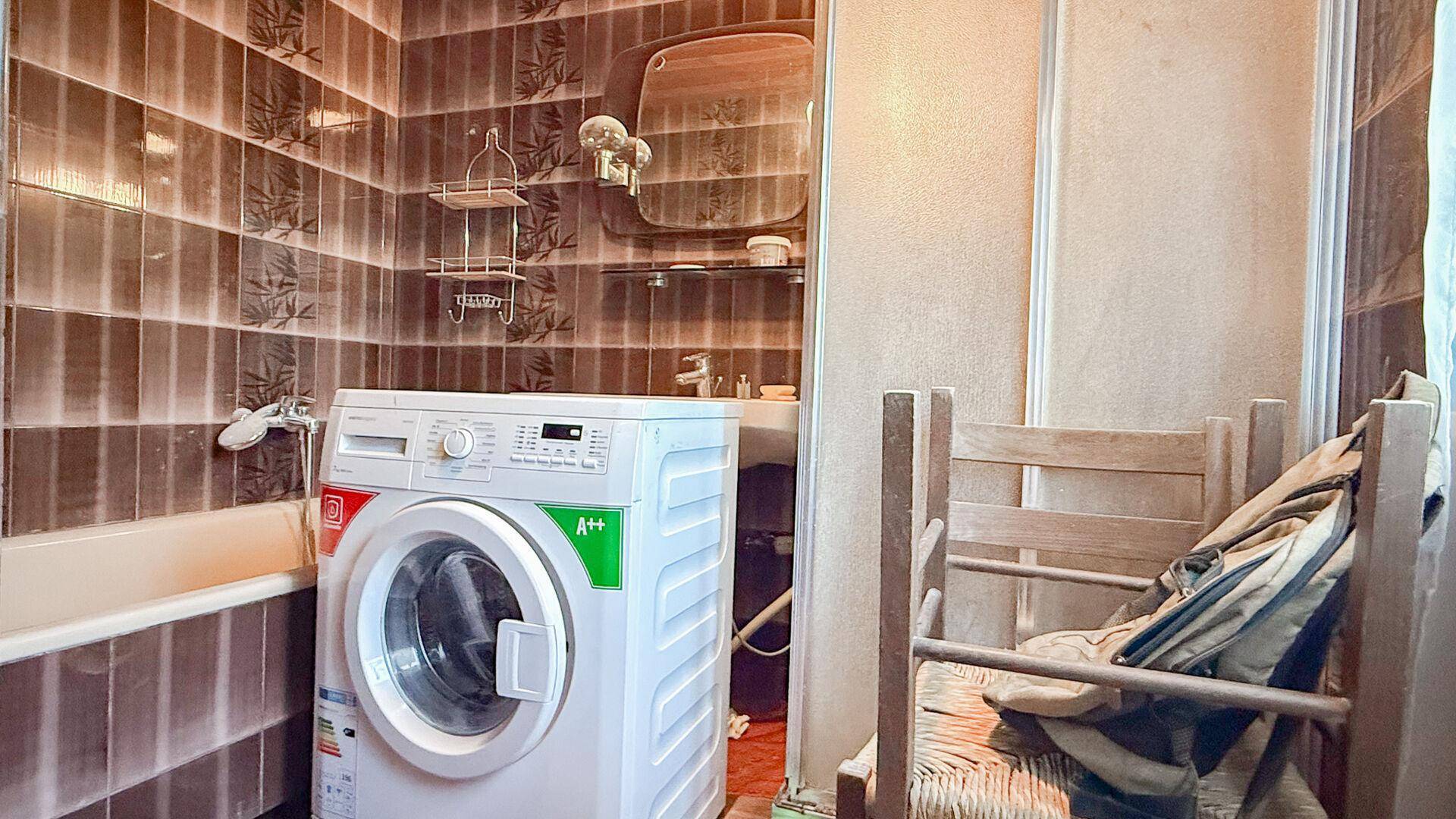 Badezimmer mit braunen Wandfliesen, Badewanne und einer modernen Waschmaschine.