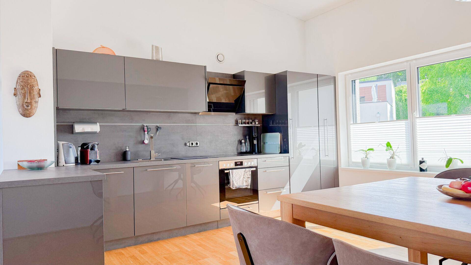 Helle, moderne Küche mit grauen Schränken, großem Fenster und Platz für einen Esstisch.
