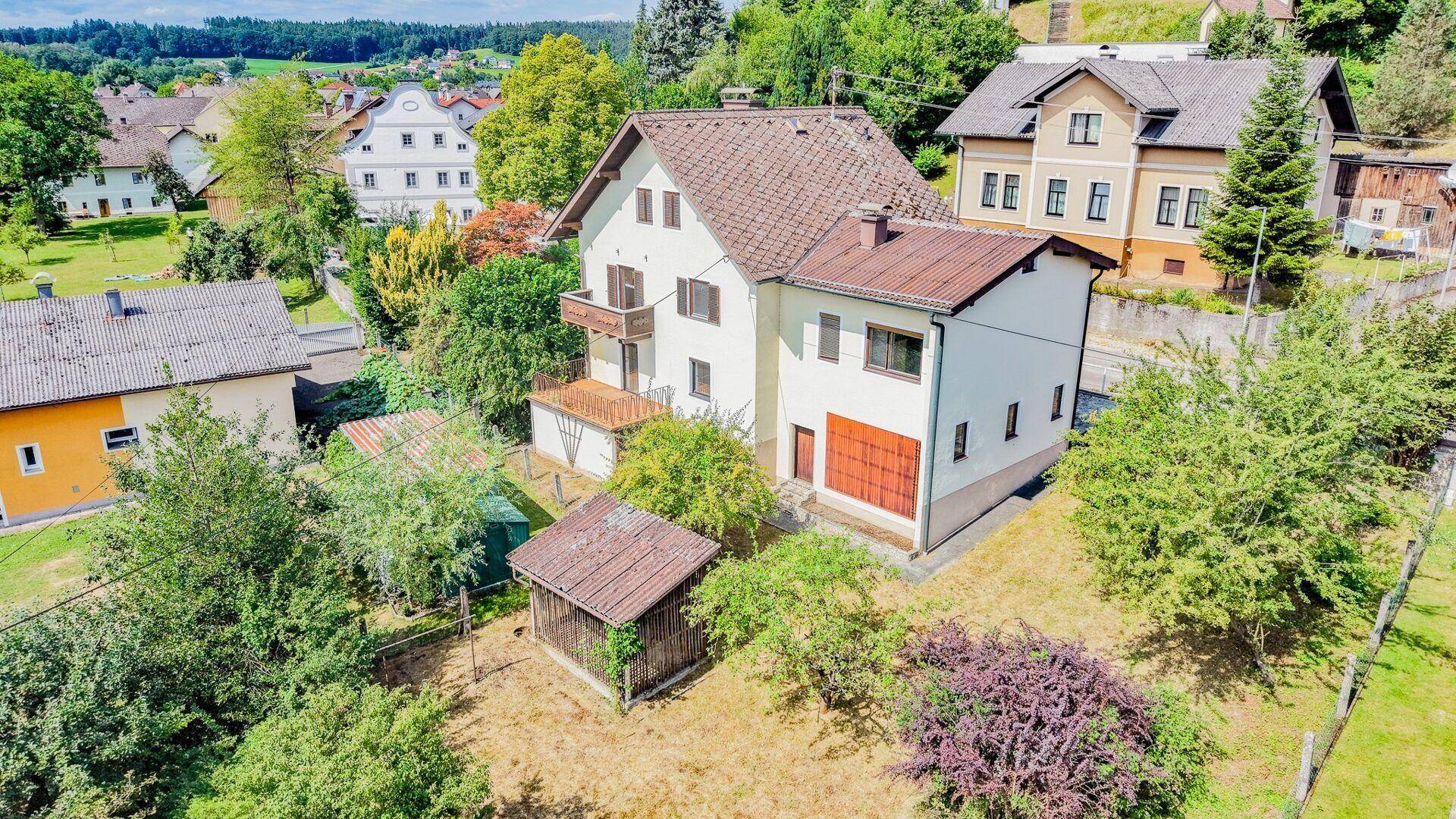 Luftaufnahme des Hauses mit braunem Dach, kleinem Schuppen und verwildertem Gartenbereich.