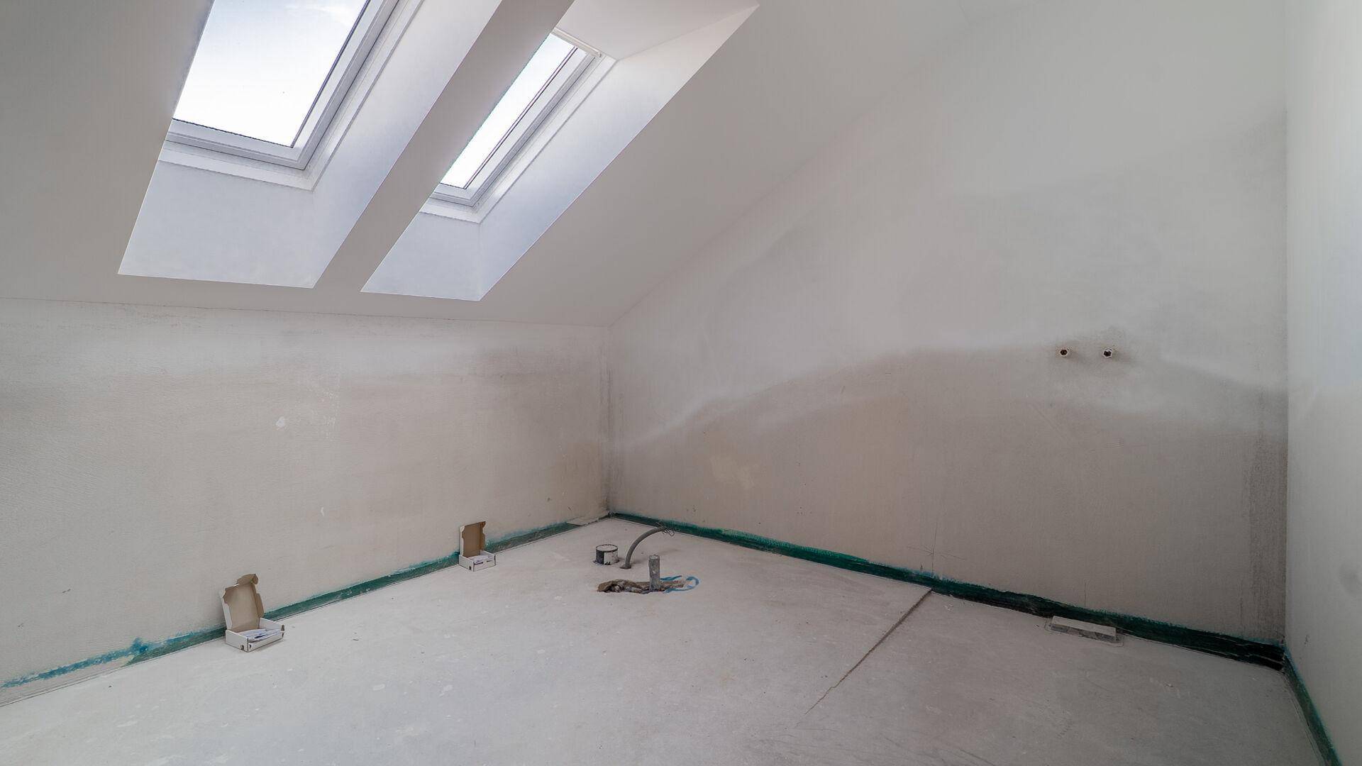 Unfertiges Badezimmer mit Dachfenstern und vorbereiteten Anschlüssen für Sanitäranlagen.