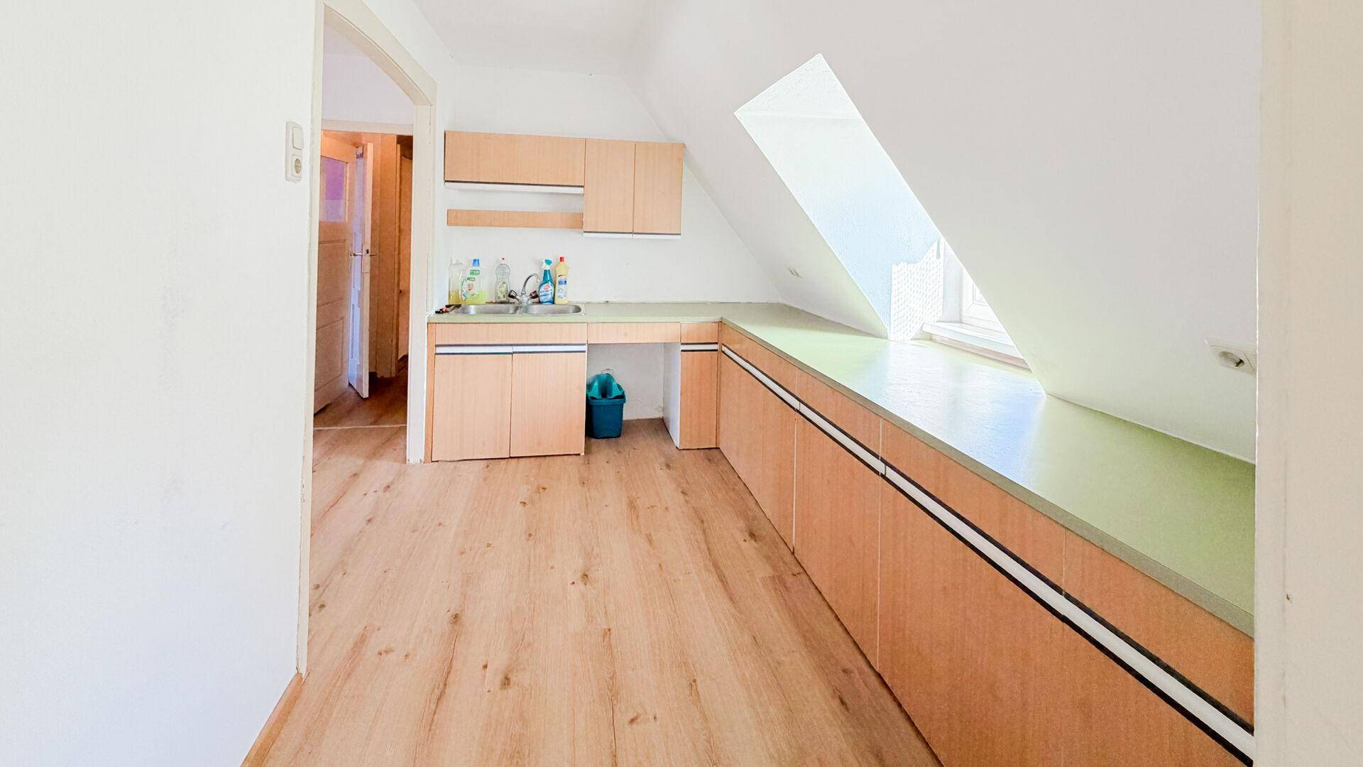 Dachgeschosszimmer mit kleiner Küchenzeile, Laminatboden und großem Dachfenster.