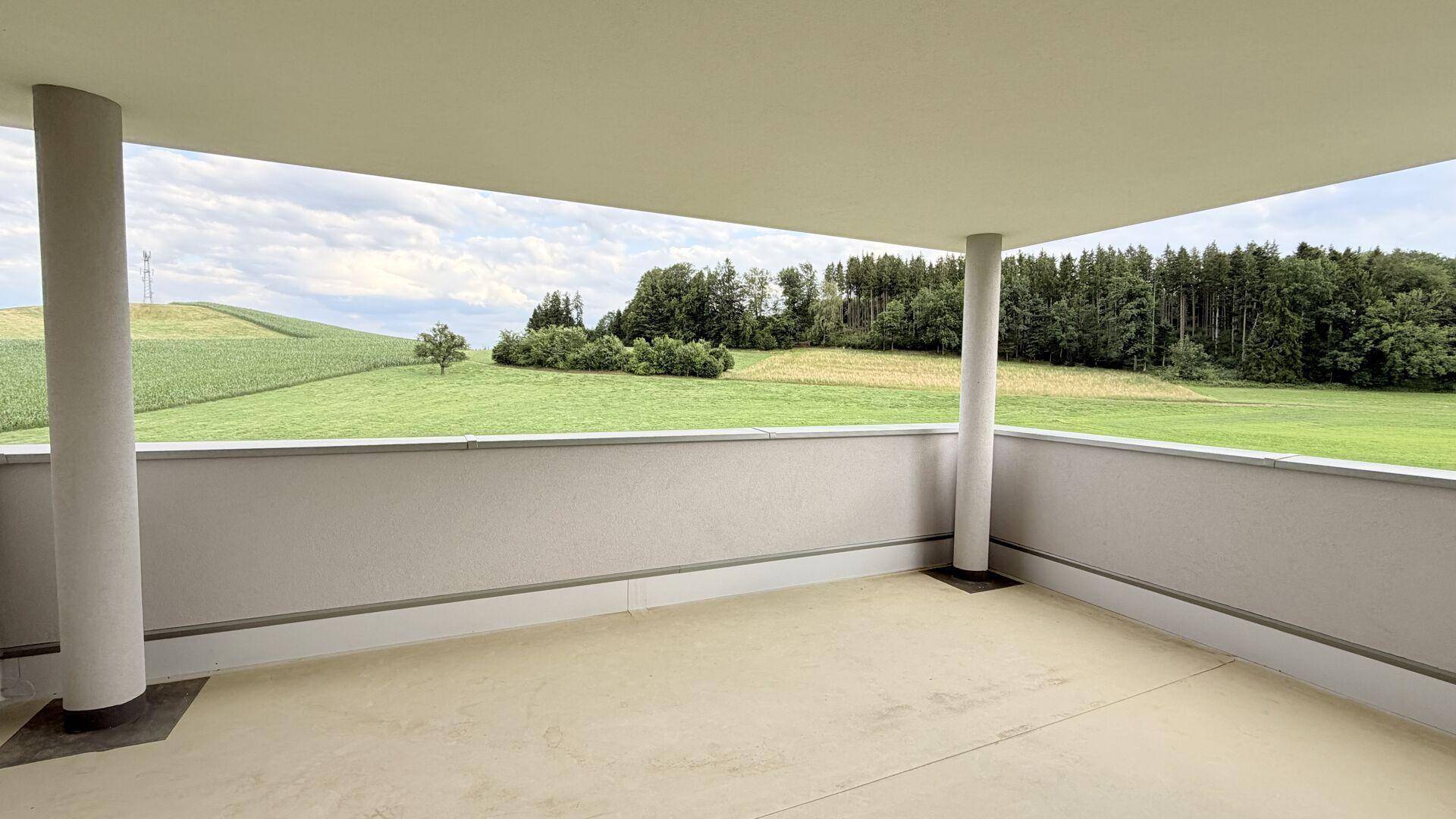 Überdachter Balkon mit Betonboden und weitem Blick über die umliegende grüne Landschaft.