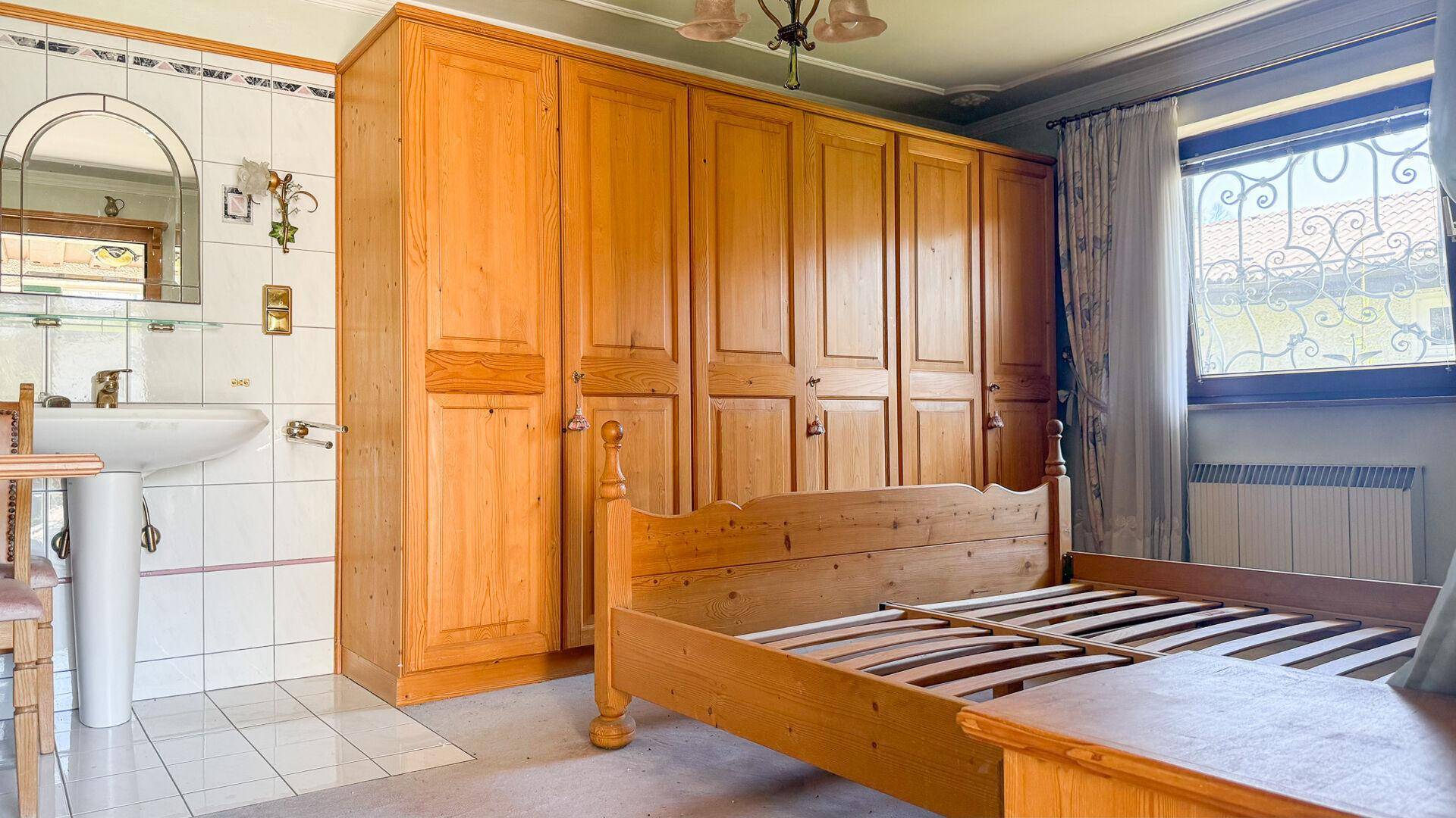 Schlafzimmer mit Holzbett, großem Kleiderschrank und integriertem Waschbecken am Fenster.