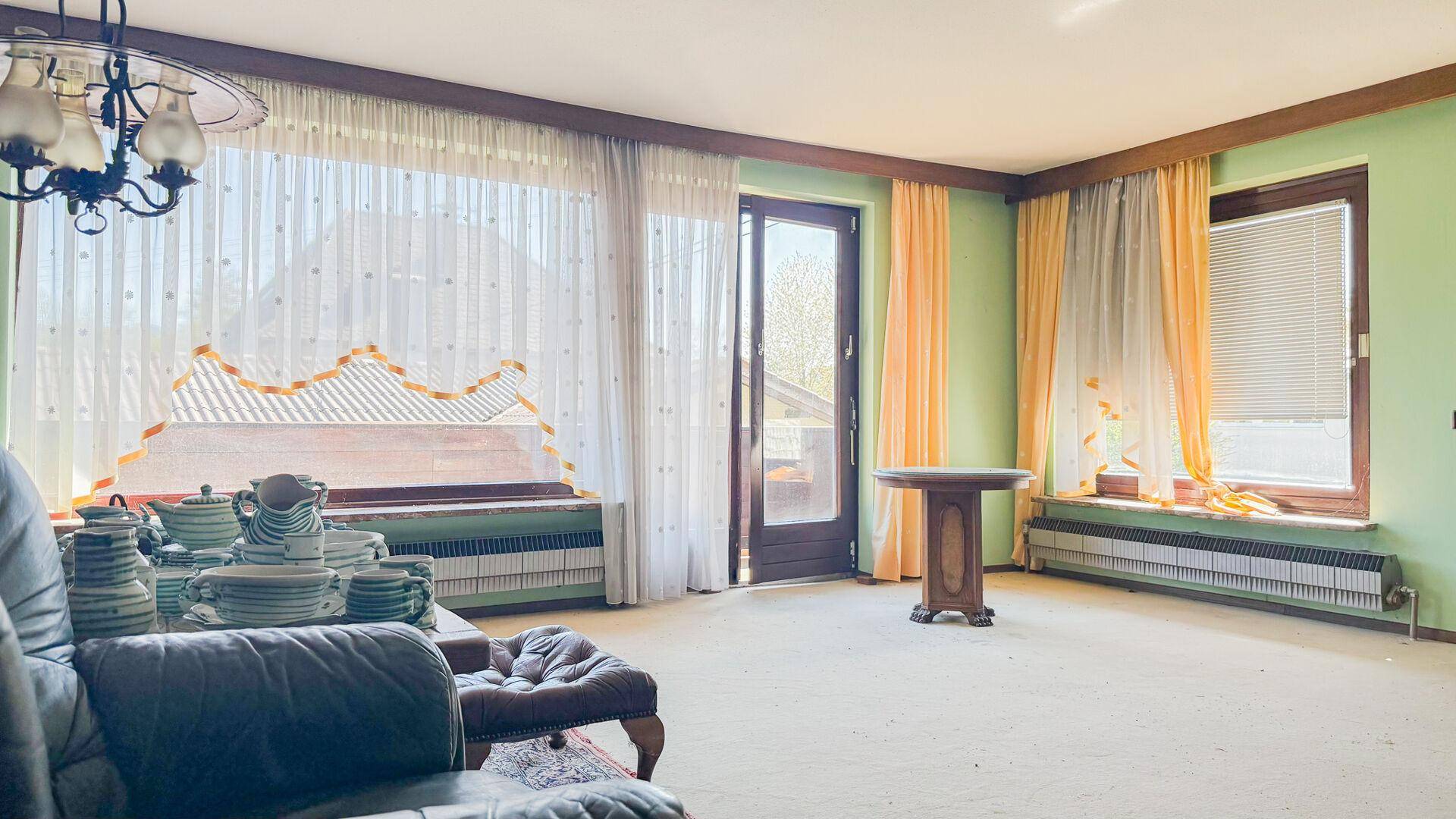 Helles Wohnzimmer mit Teppichboden und Zugang zu einem Balkon, gut belichtet durch große Fenster.