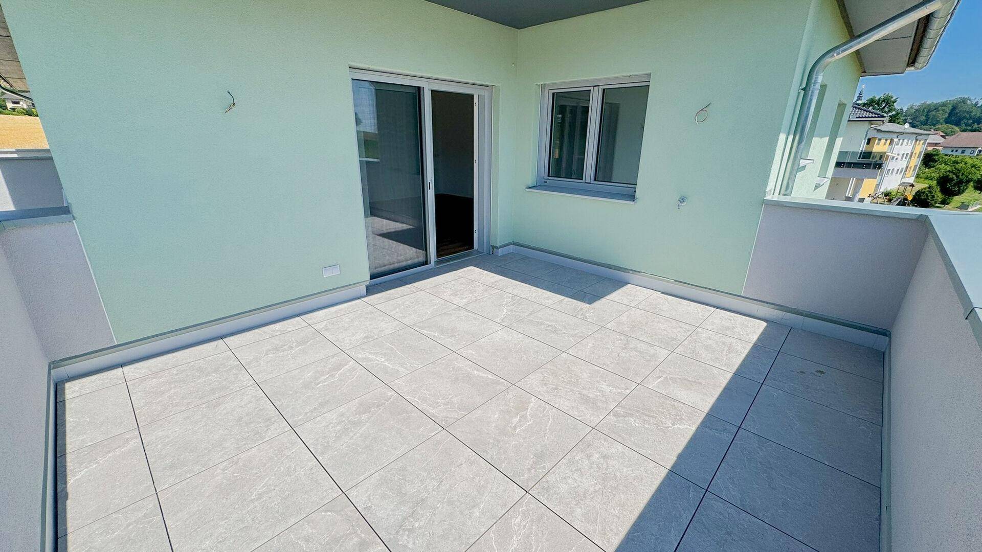 Große geflieste Terrasse mit Schiebetürzugang und Blick auf die Umgebung.