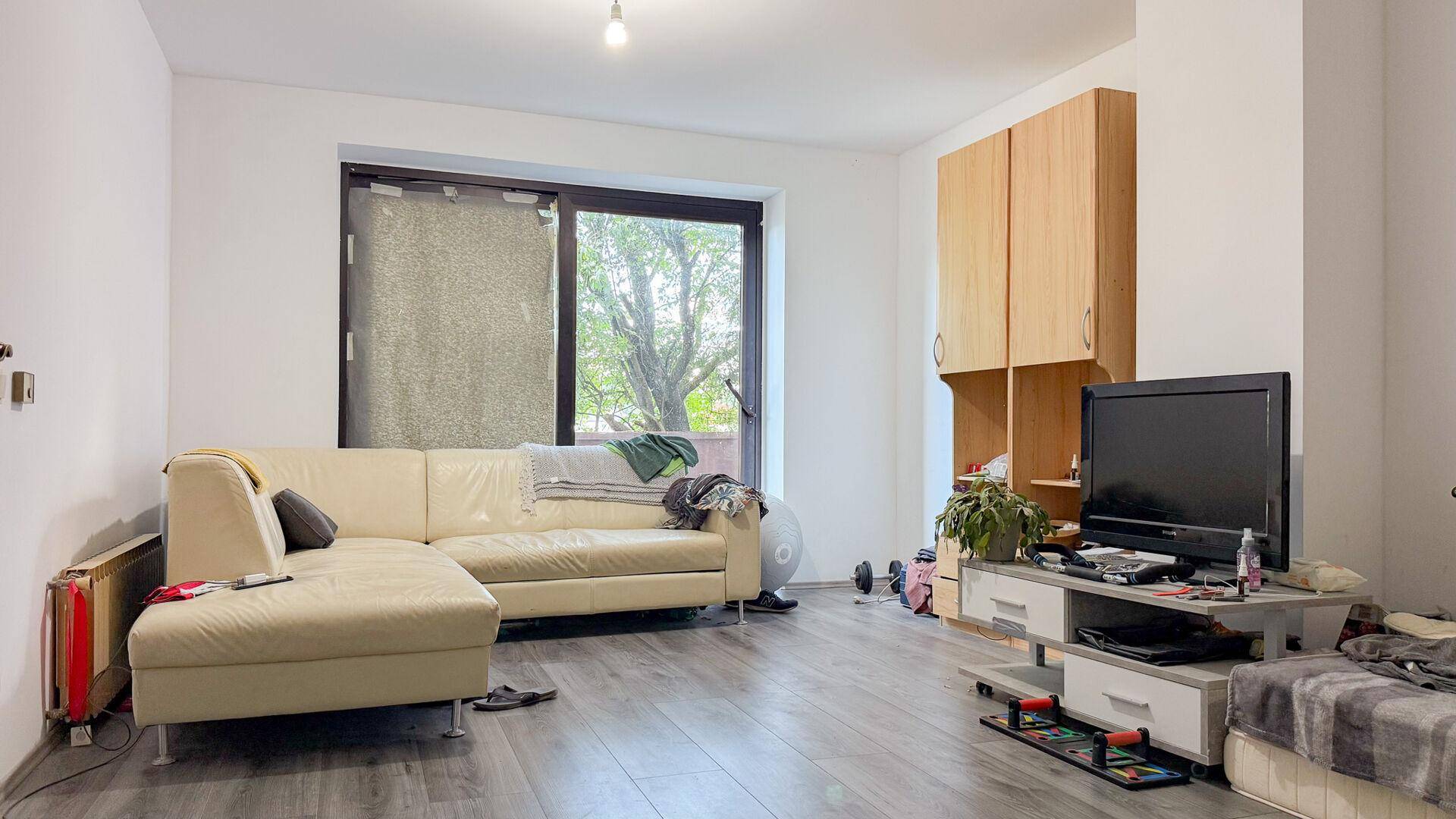 Wohnzimmer mit hellem Sofa, Fernseher und großem Fenster mit Blick ins Grüne.