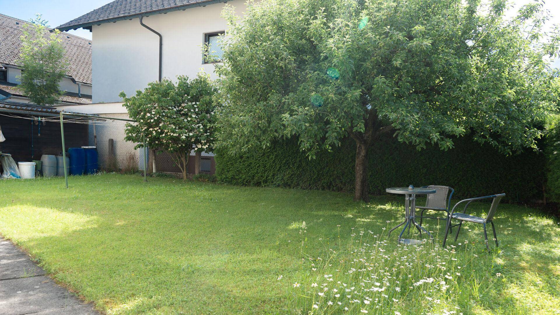 Großer grüner Garten mit Rasen, Bäumen und einer kleinen Sitzgruppe im Freien.
