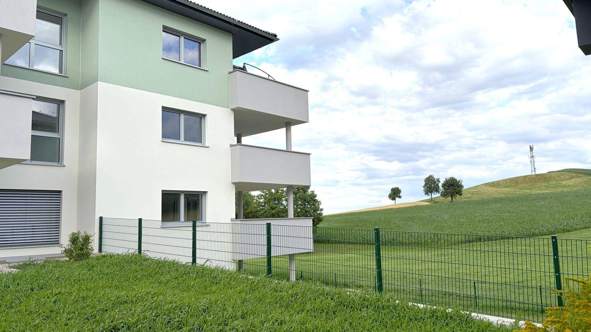 Moderne Wohnhausfassade in Grün und Weiß mit Balkonen und Blick auf die umliegende Natur.