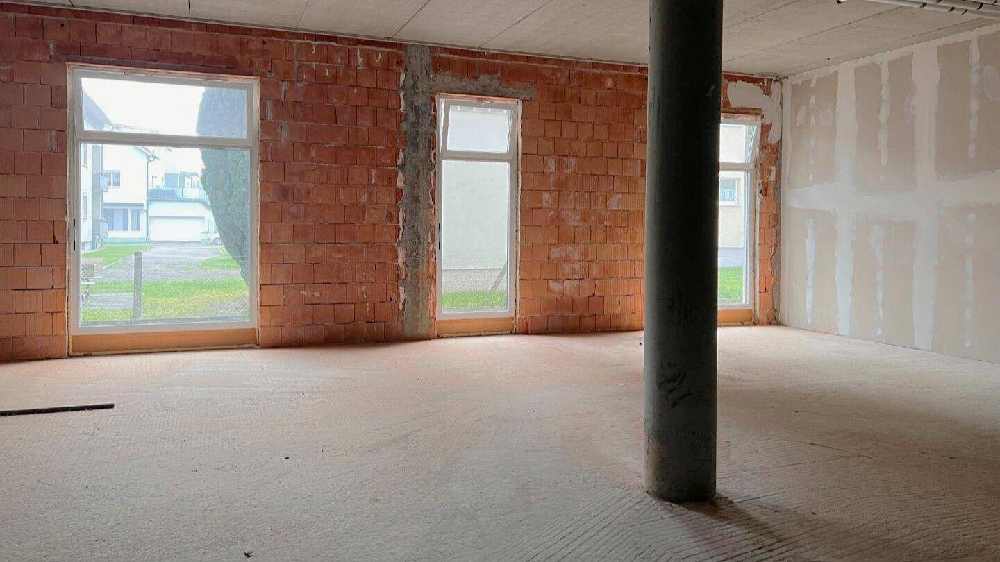Unfertiger Innenraum mit unverputzten Ziegelwänden und Rohbetonboden während der Bauphase.