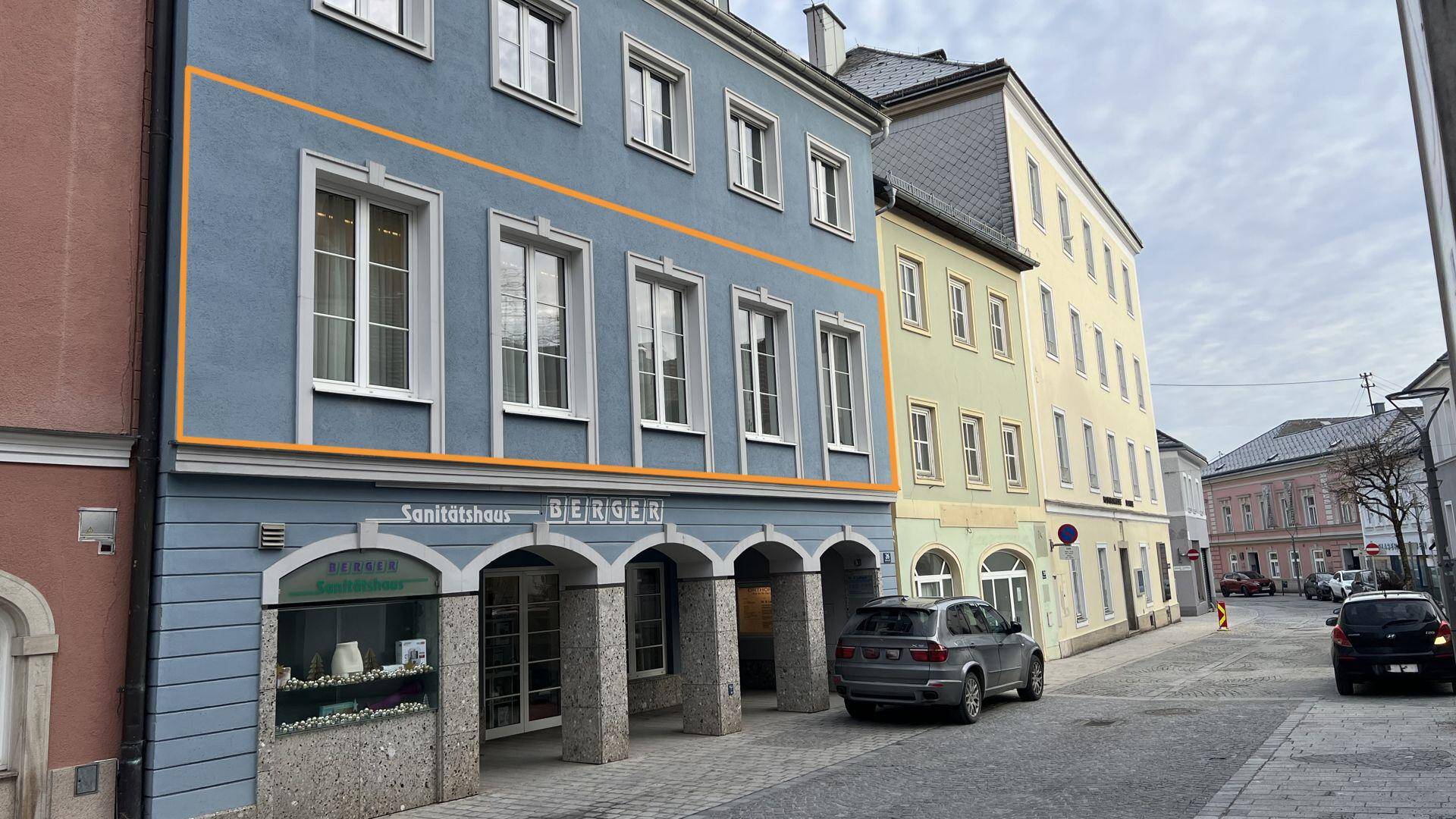 Historisches Gebäude mit blauer Fassade und orangefarbener Markierung, an einer belebten Straße gelegen.