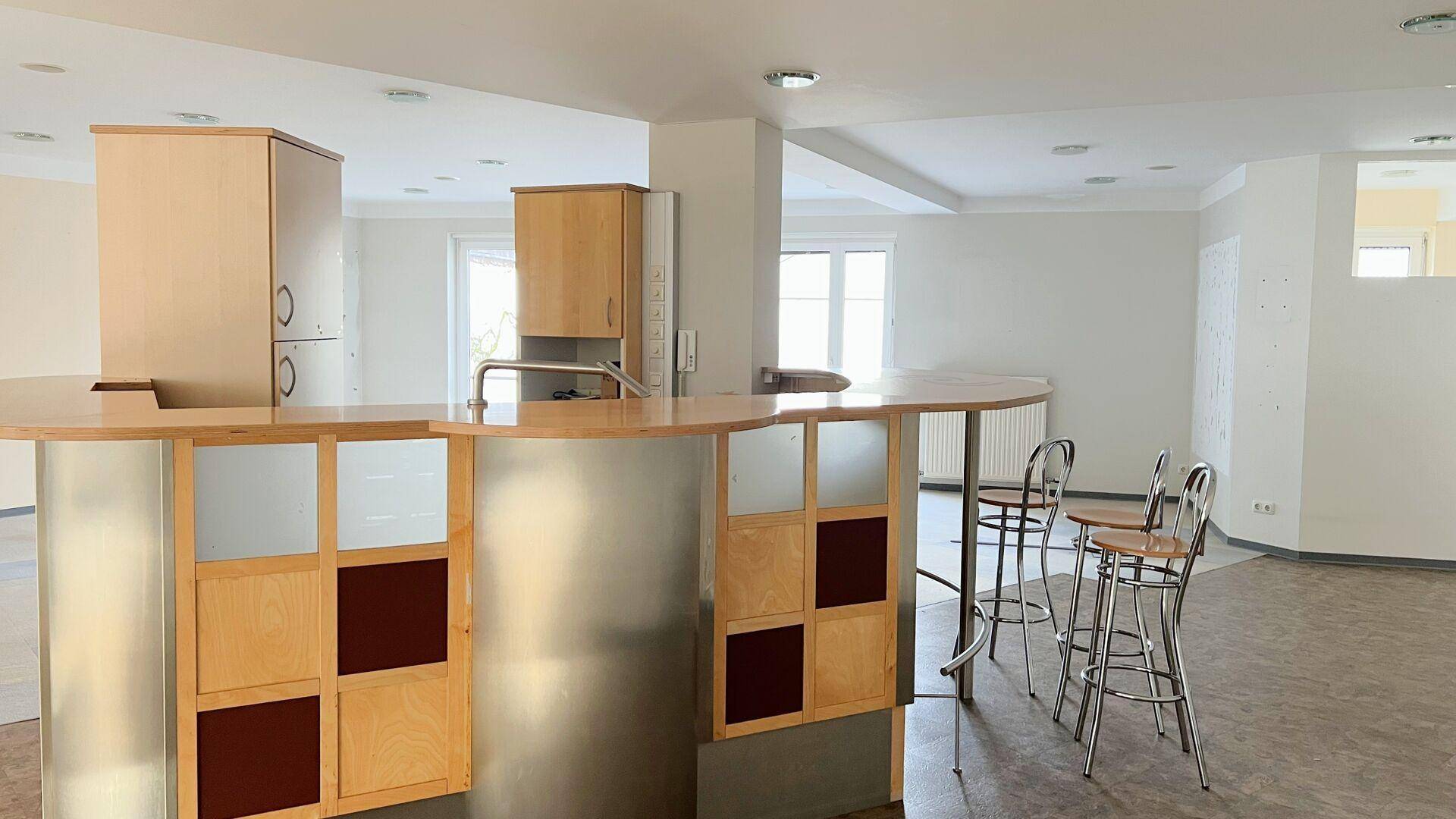 Detailansicht der Bar mit Holz- und Metallverkleidung sowie passenden Barhockern in einem offenen Raum.