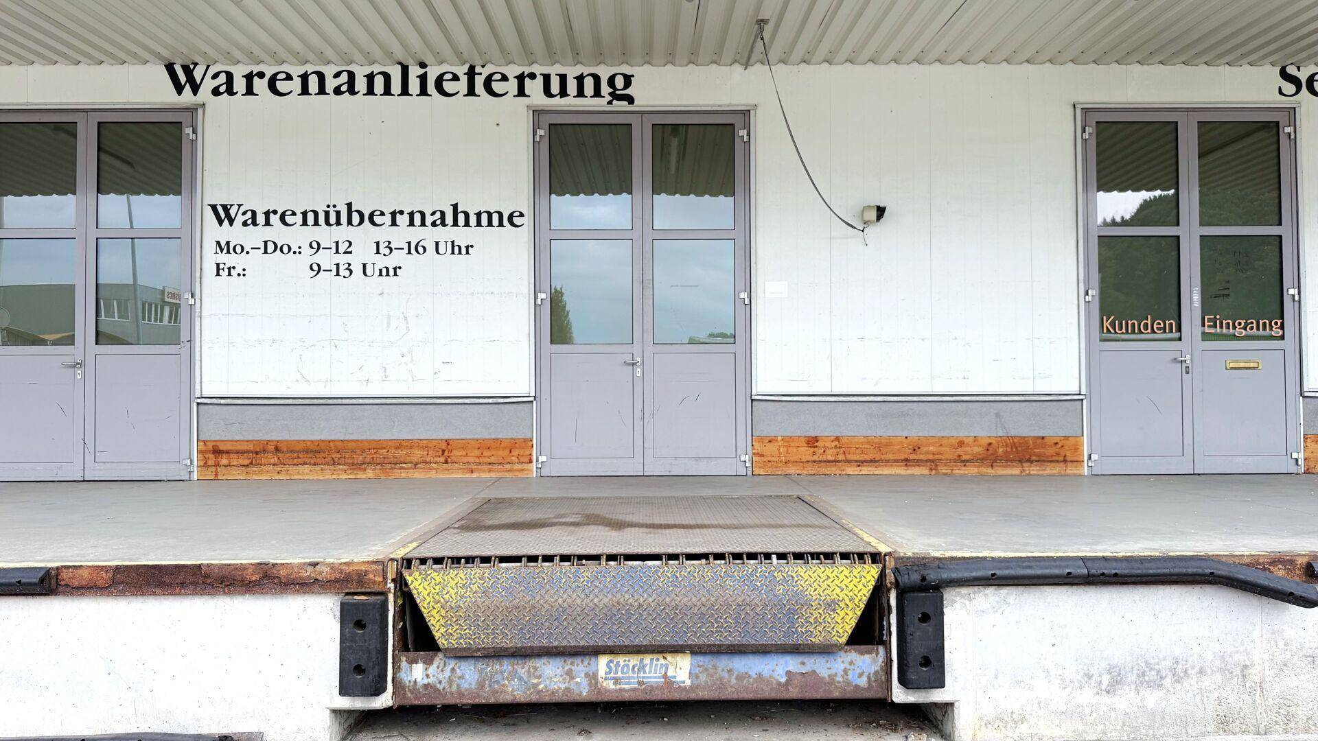 Nahaufnahme der Laderampe mit Türen und Beschriftungen für Warenanlieferung und -übernahme.