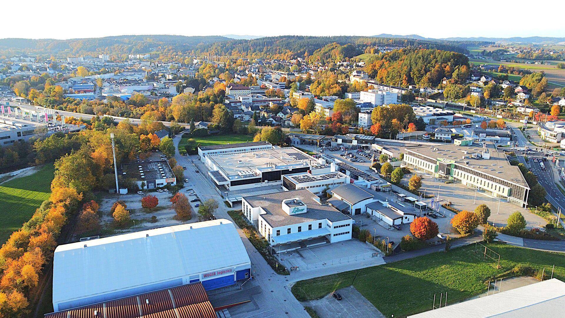 Weitläufige Luftaufnahme eines Gewerbegebiets umgeben von herbstlicher Landschaft und Wohngebieten.