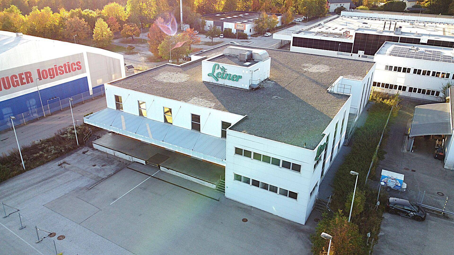 Luftaufnahme des Gewerbegebäudes mit angrenzendem Logistikzentrum und Herbstbäumen.