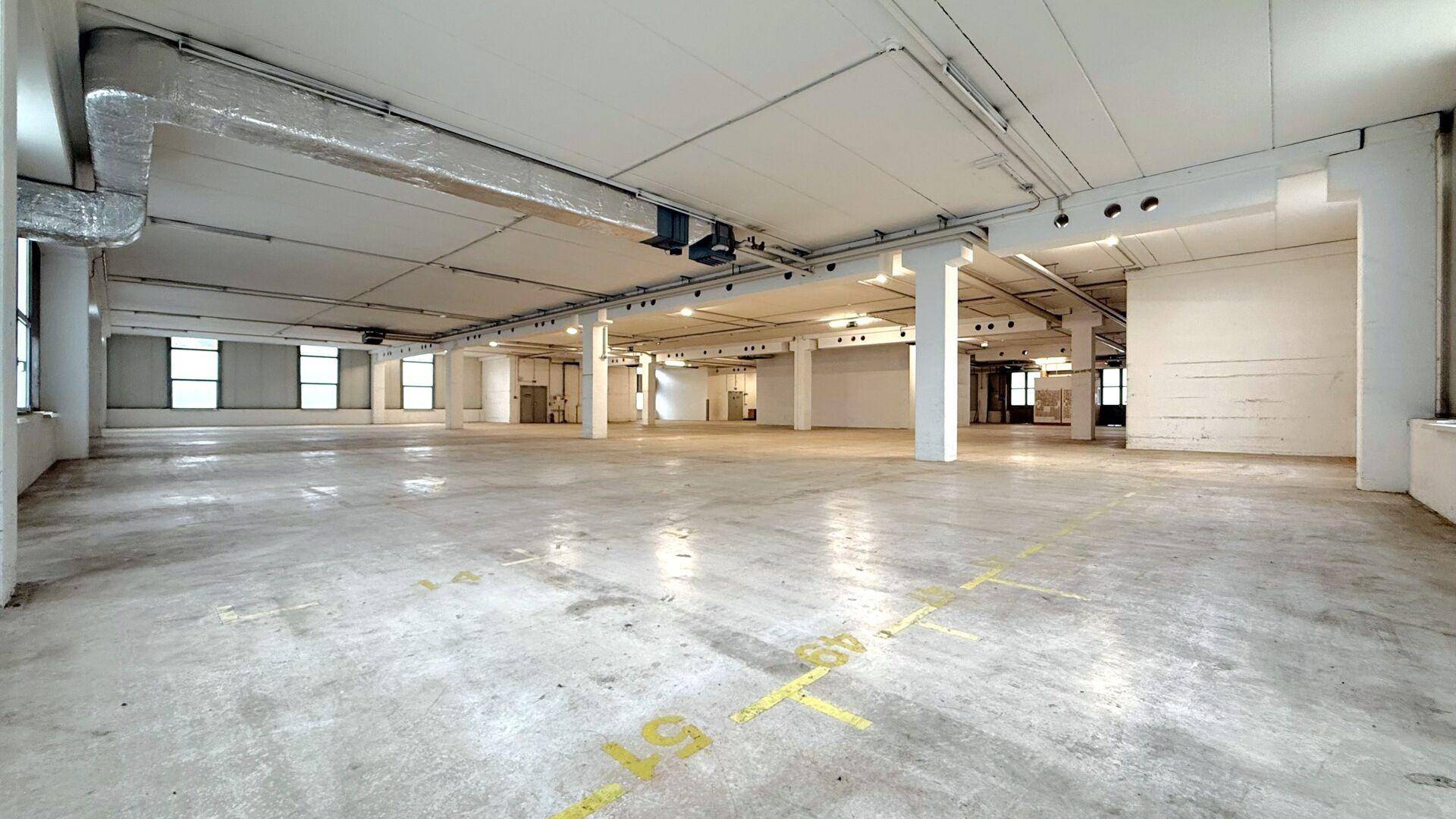 Weitläufiger, heller Lagerraum mit vielen Fenstern und industrieller Deckenkonstruktion.
