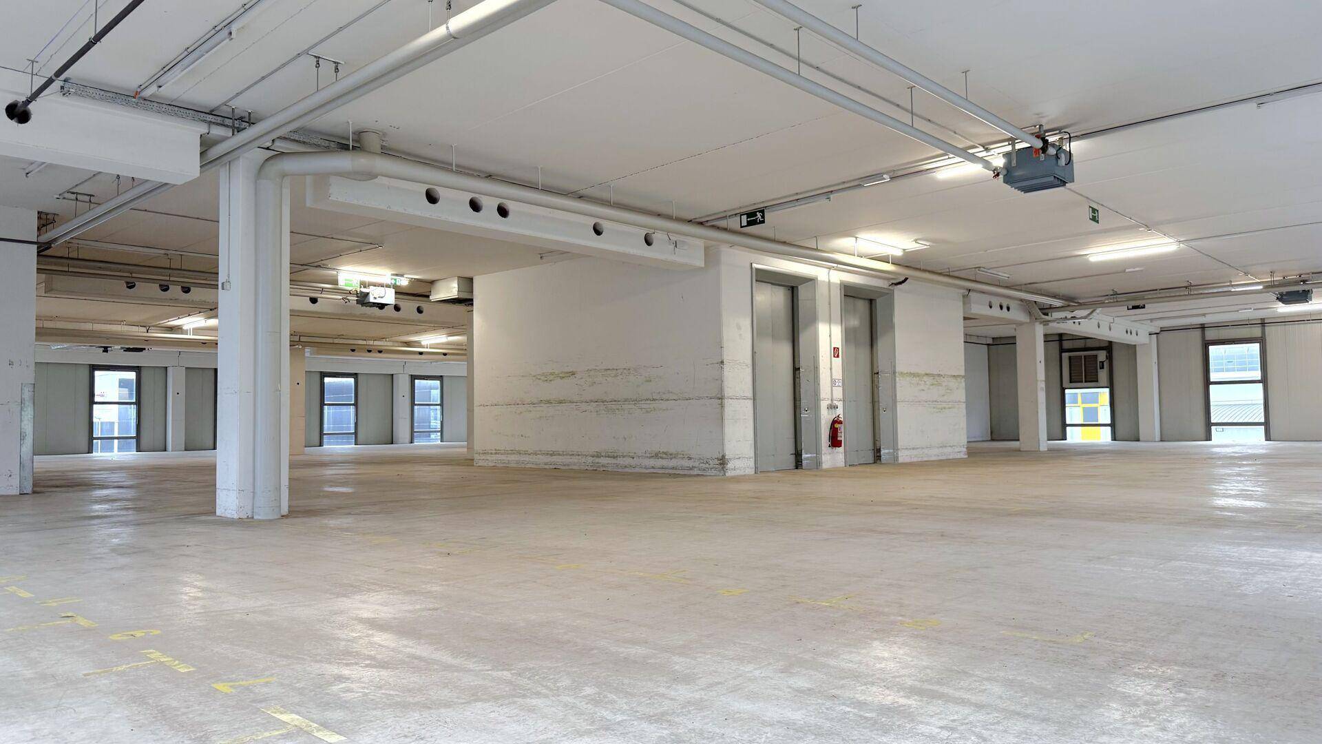 Offener Lagerraum mit Betonboden, Säulen und Blick auf die Aufzüge im Hintergrund.