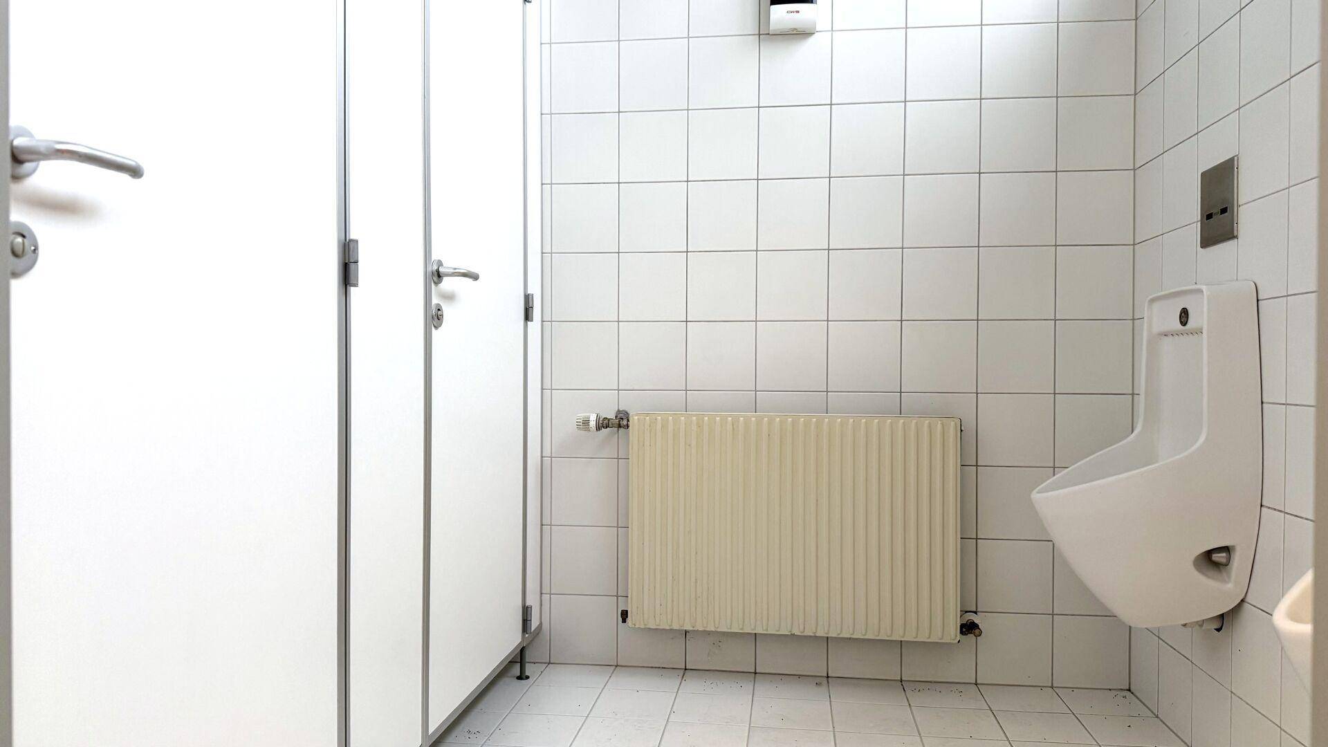 Herren-Waschraum mit weißen Fliesen, Urinalen und Trennwänden.