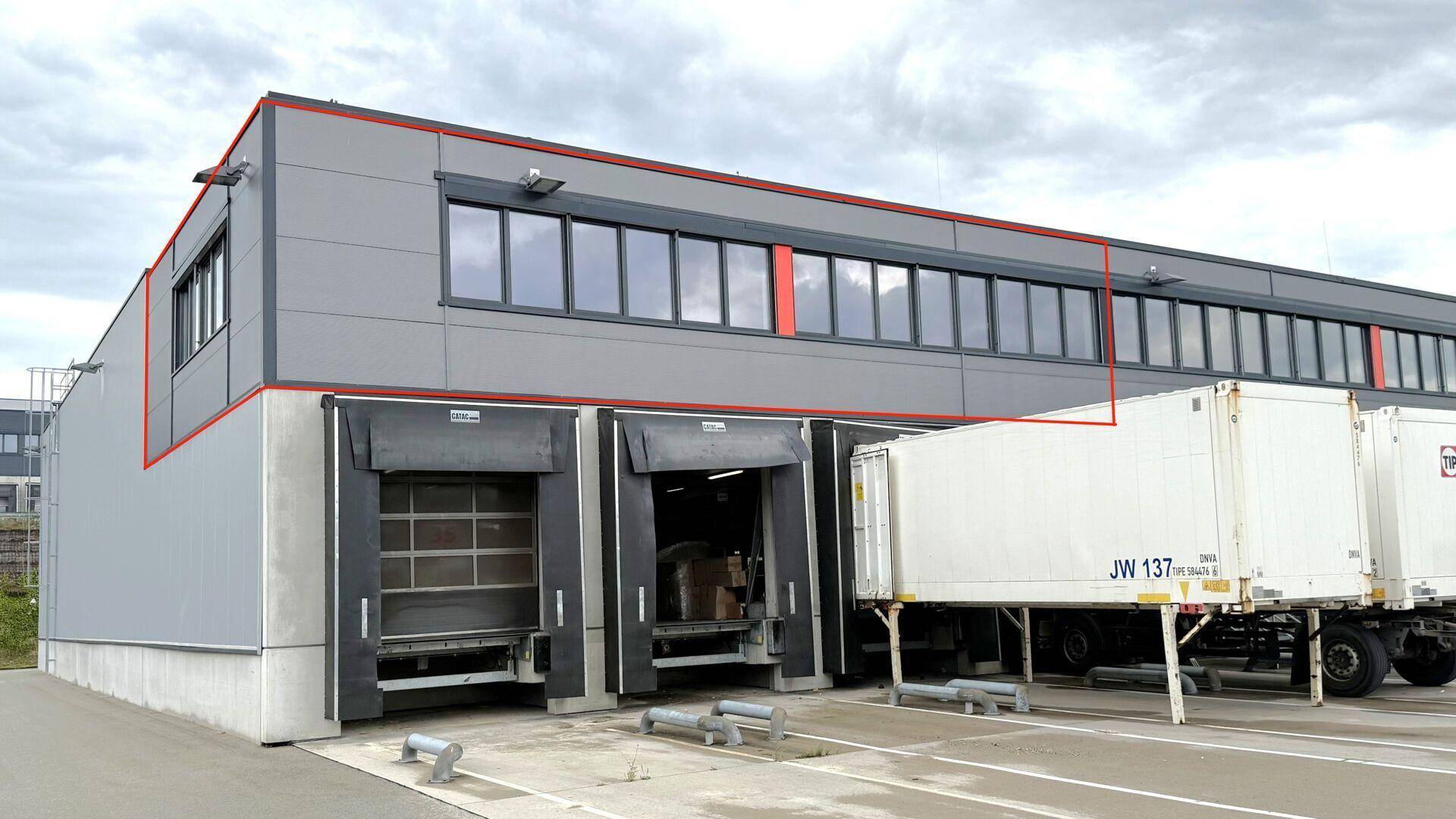 Modernes Industriegebäude mit Laderampen und großen Fenstern, umgeben von Lastwagen.