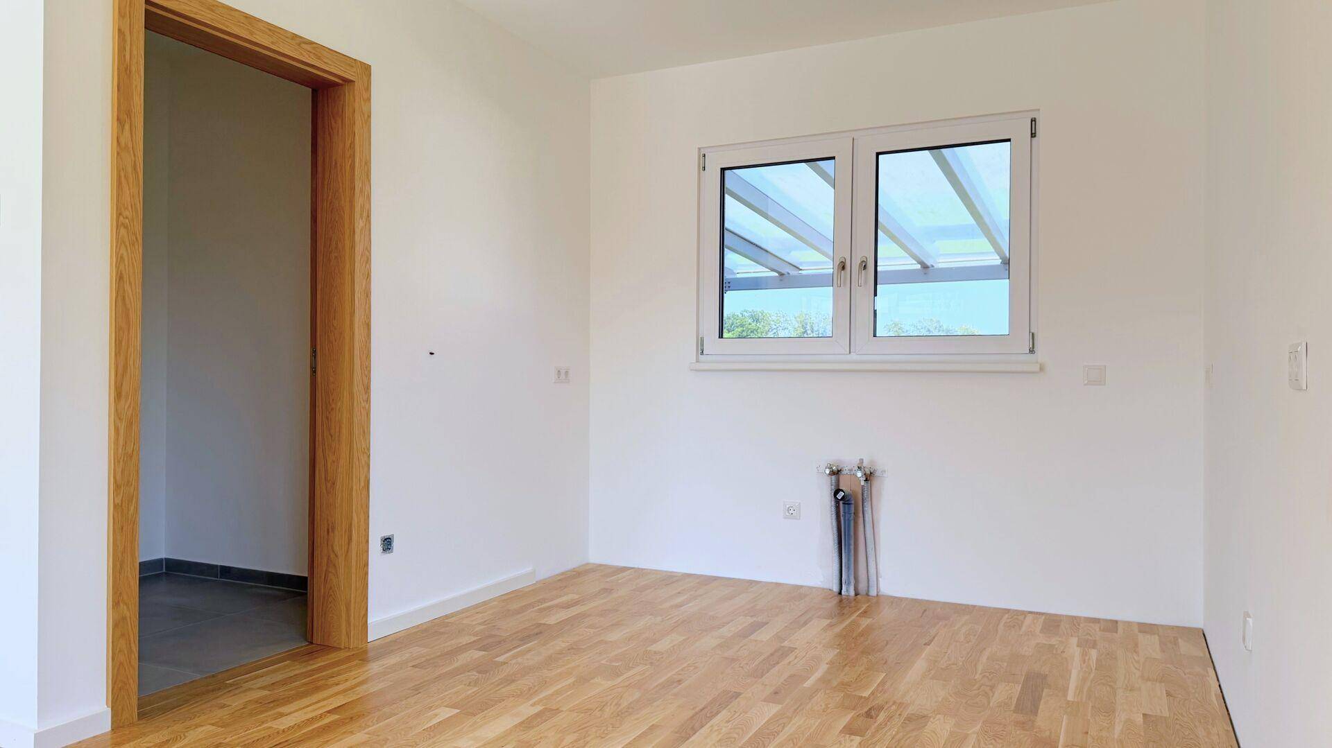 Leerer Raum mit Holzboden und Fenster, vorbereitet für die Installation von Heizkörpern.