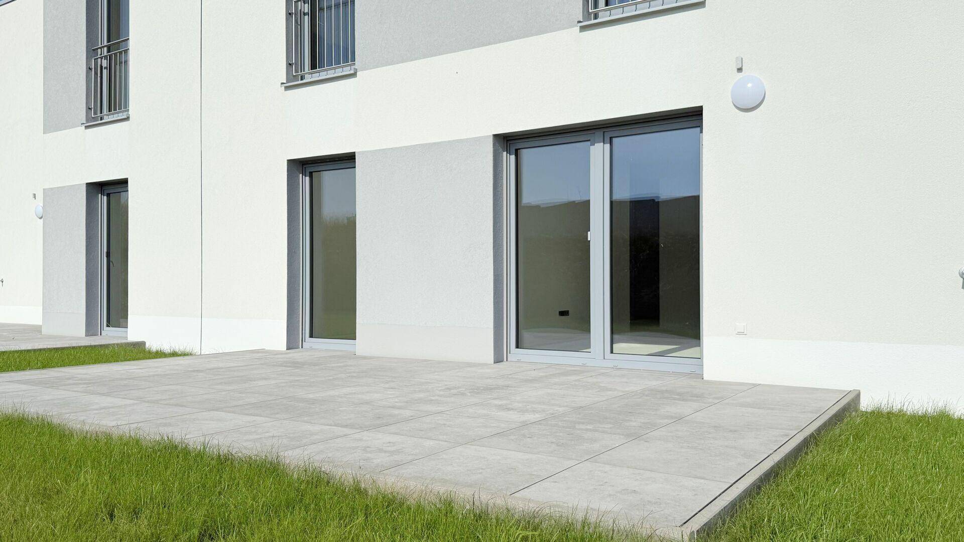 Eine gepflasterte Terrasse im Erdgeschoss mit Zugang zu einem hellen Innenraum.