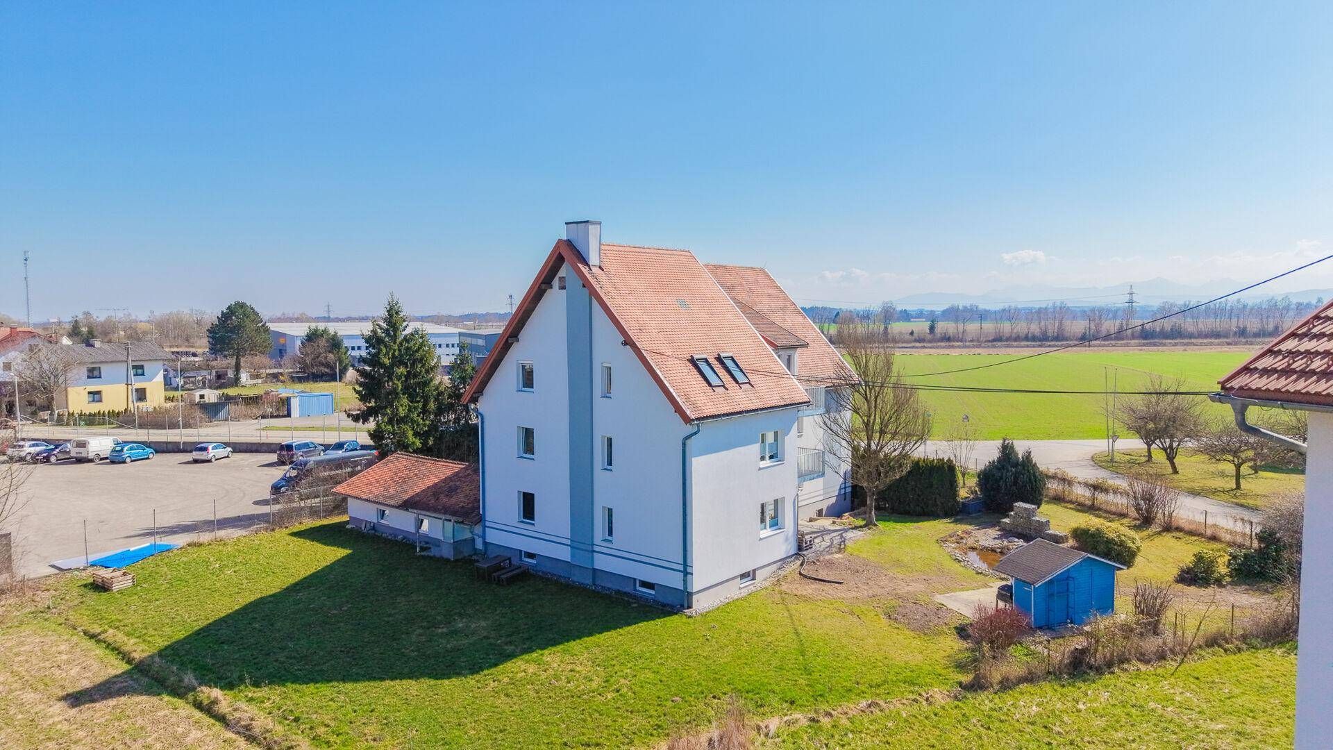 Seitenansicht des Wohnhauses aus der Vogelperspektive mit Garten, Teich und angrenzenden Feldern.