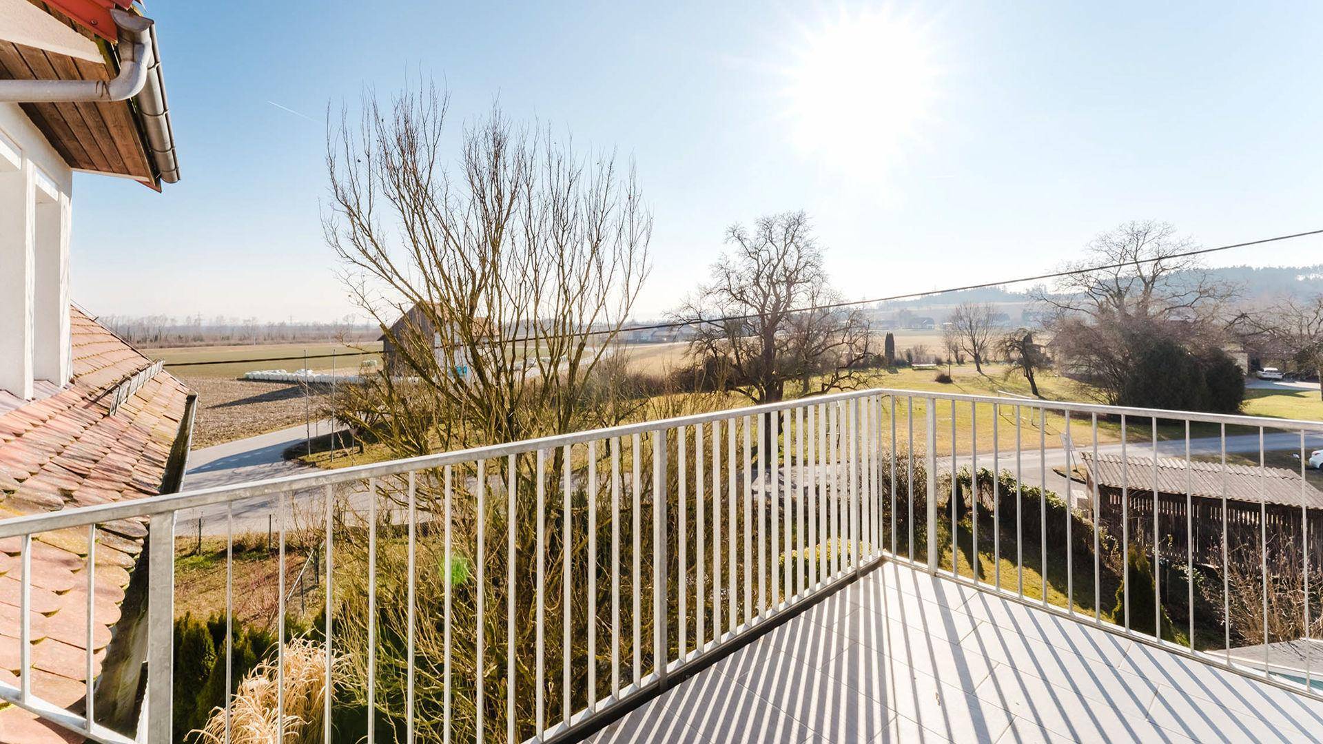 Heller Balkon mit weitem Blick über die ländliche Umgebung unter strahlendem Sonnenschein.