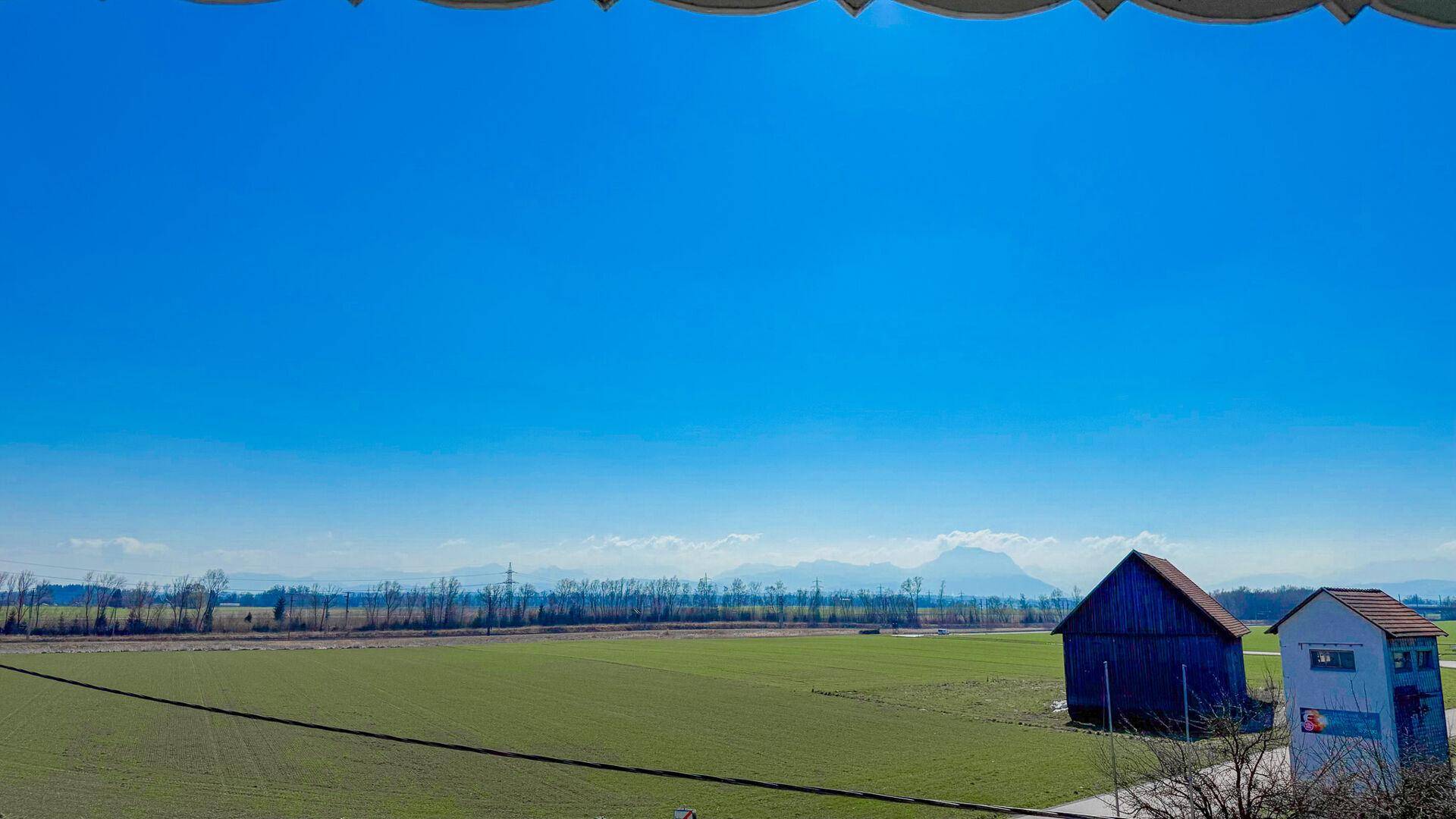 Panoramablick über weite grüne Felder und die umliegende Landschaft mit fernen Bergen.