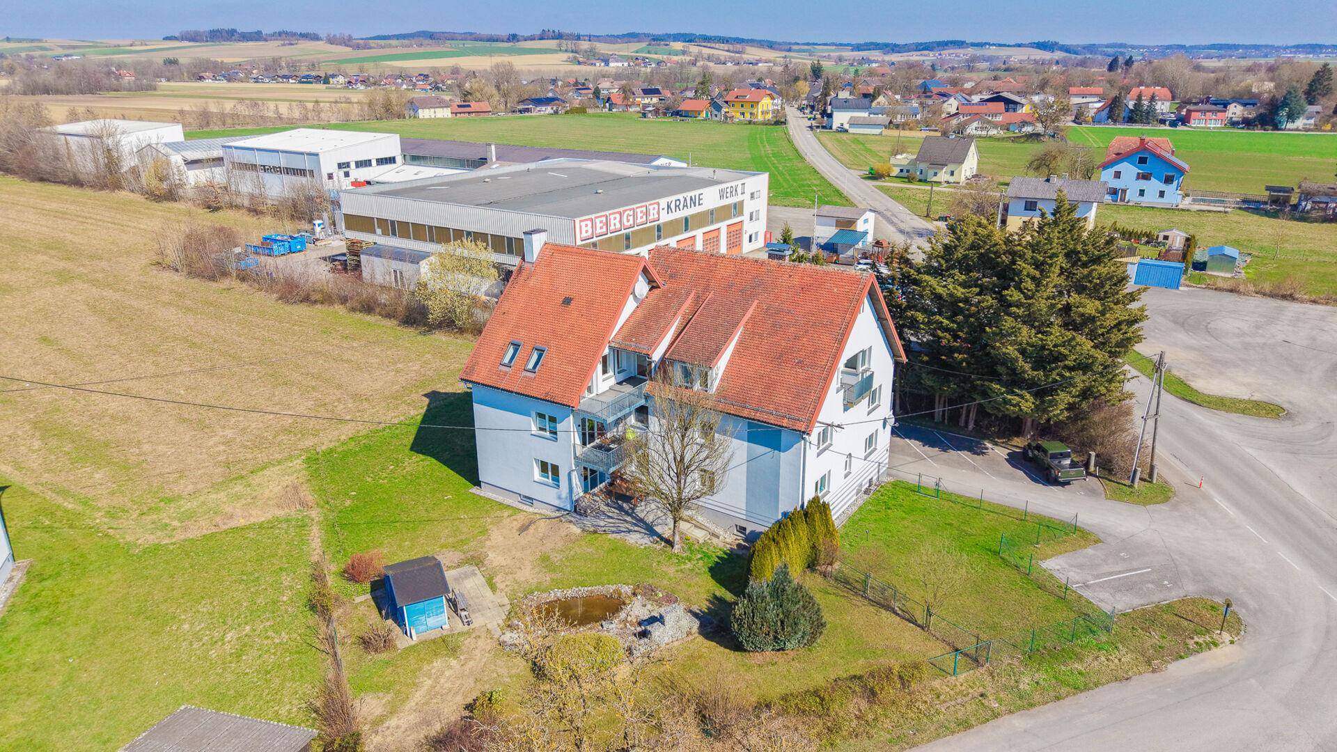 Luftaufnahme des Wohnhauses mit rotem Ziegeldach, Balkonen und umliegenden Grünflächen.