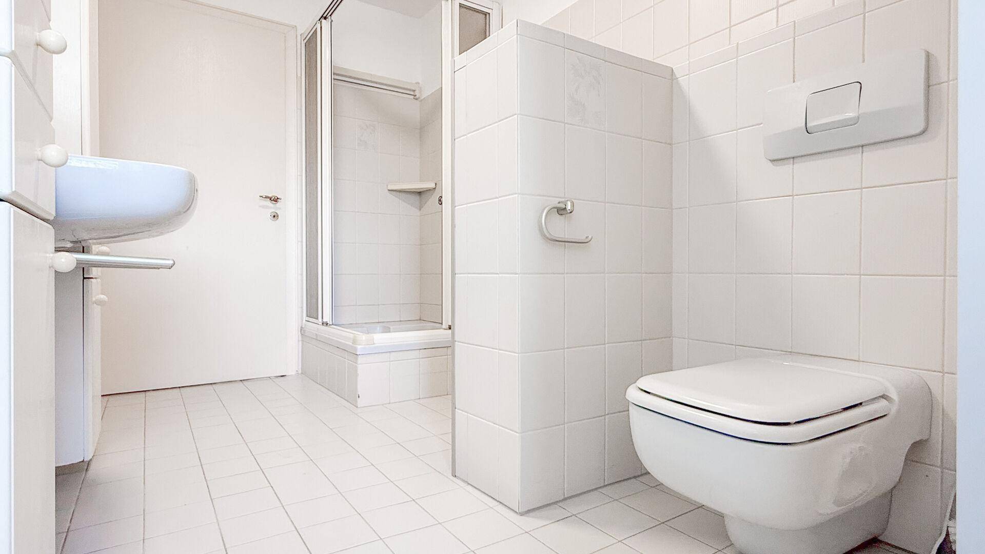 Modernes Badezimmer mit weißen Fliesen, Waschtisch, wandhängender Toilette und Duschkabine.