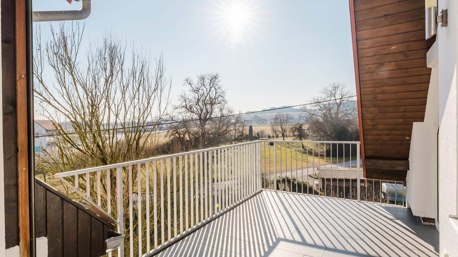 Geräumiger Balkon mit sonnigem Ausblick auf Bäume und die hügelige Landschaft.