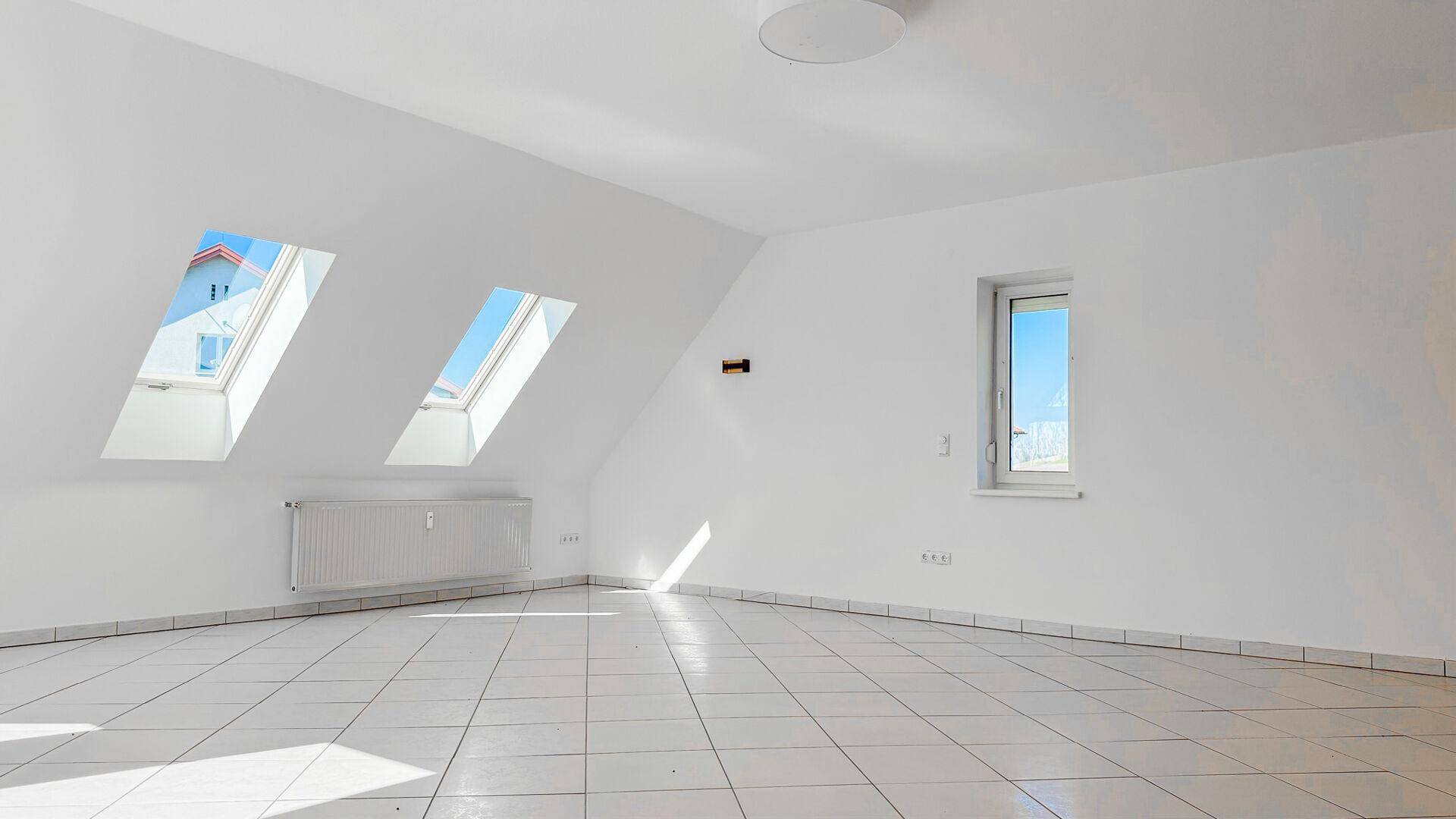 Geräumiges Dachgeschosszimmer mit viel Tageslicht durch mehrere Dachfenster und einem Fenster.
