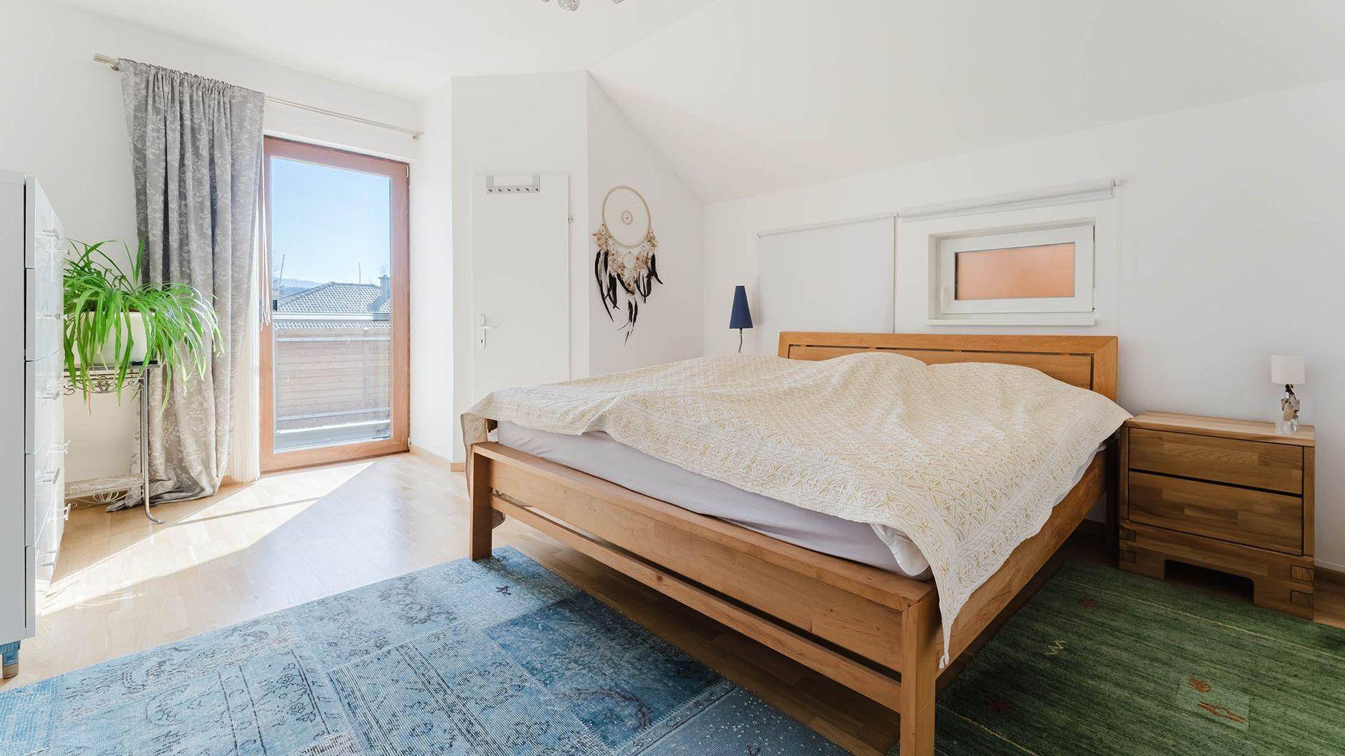 Helles Schlafzimmer mit Holzbett, Nachttischen und Zugang zu einem Außenbereich.