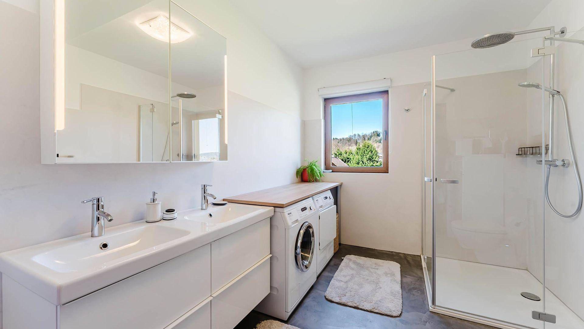 Modernes Badezimmer mit Doppelwaschbecken, begehbarer Dusche, Waschmaschine und Fenster.