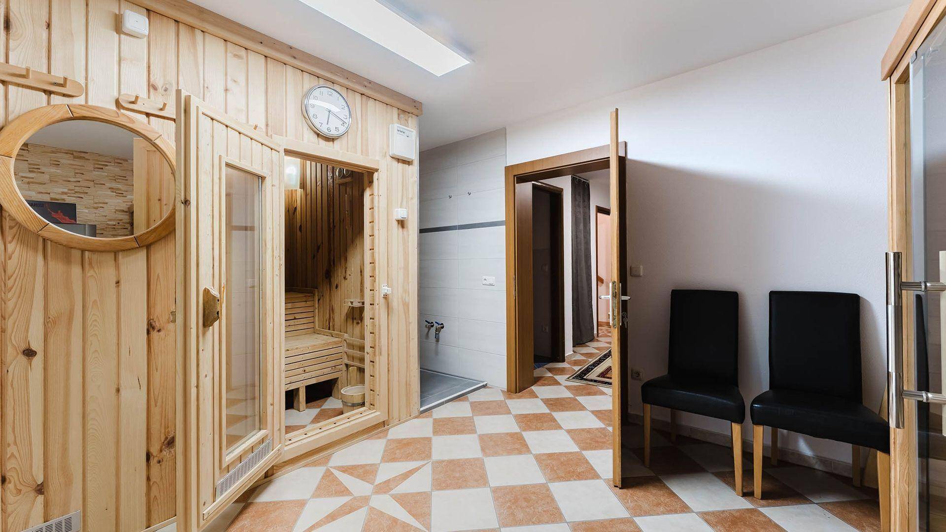 Entspannender Wellnessbereich mit holzverkleideter Sauna, Dusche und Sitzgelegenheiten.