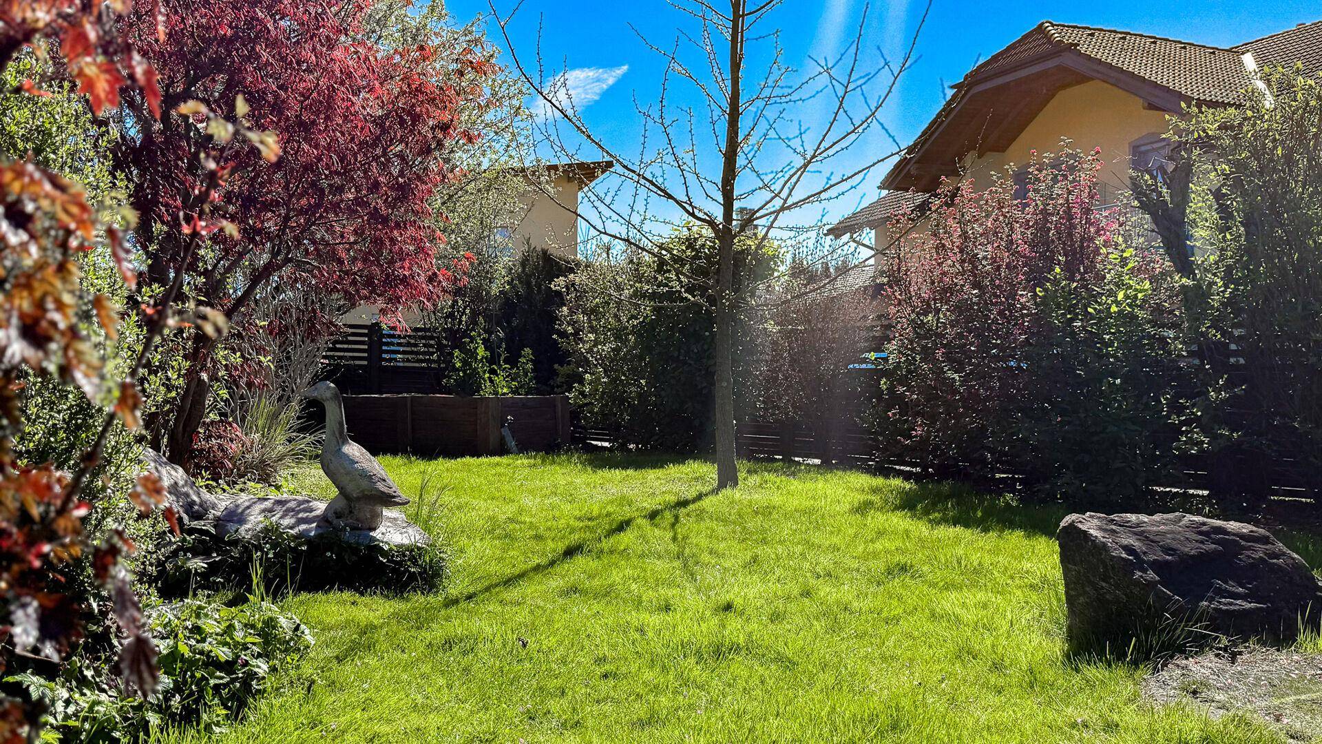 Grüner Garten mit Rasen, Bäumen und einer dekorativen Gans-Statue, im Hintergrund Häuser.