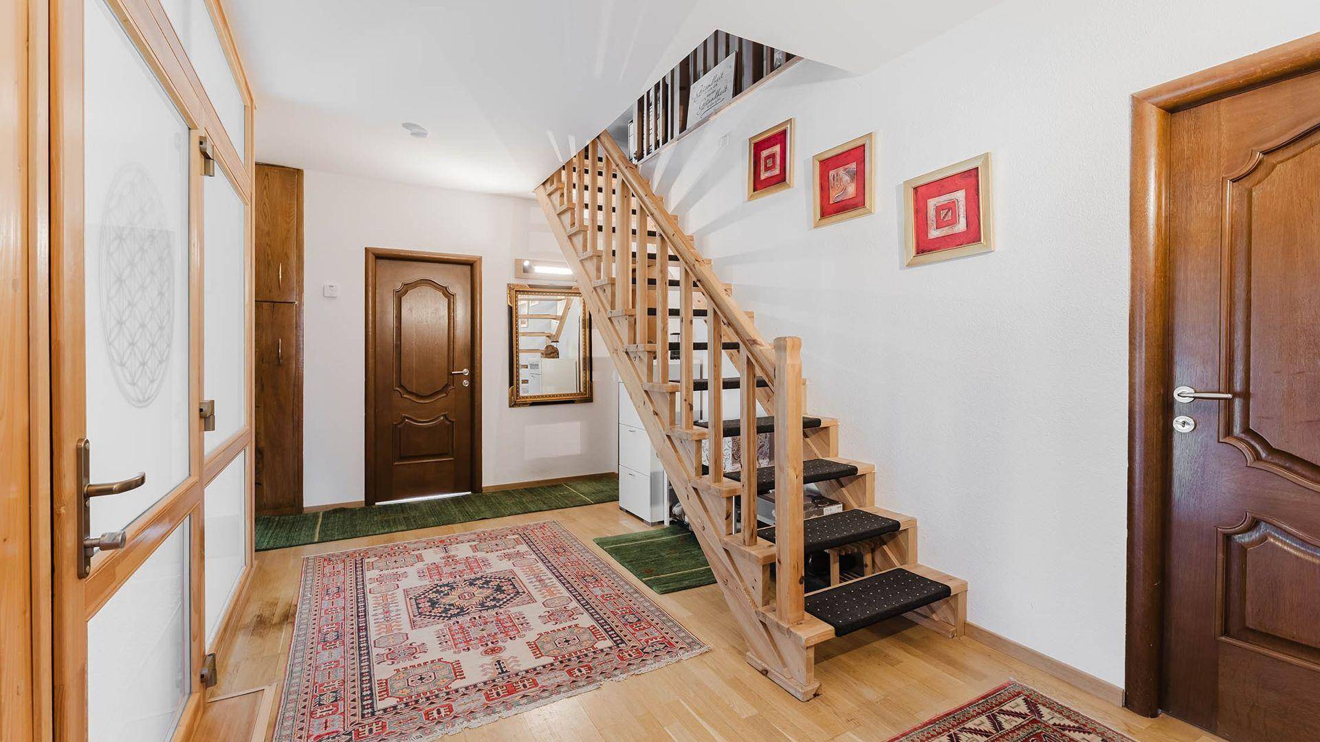 Heller Flur mit Holztreppe, Holztüren und einem gemusterten Teppich.