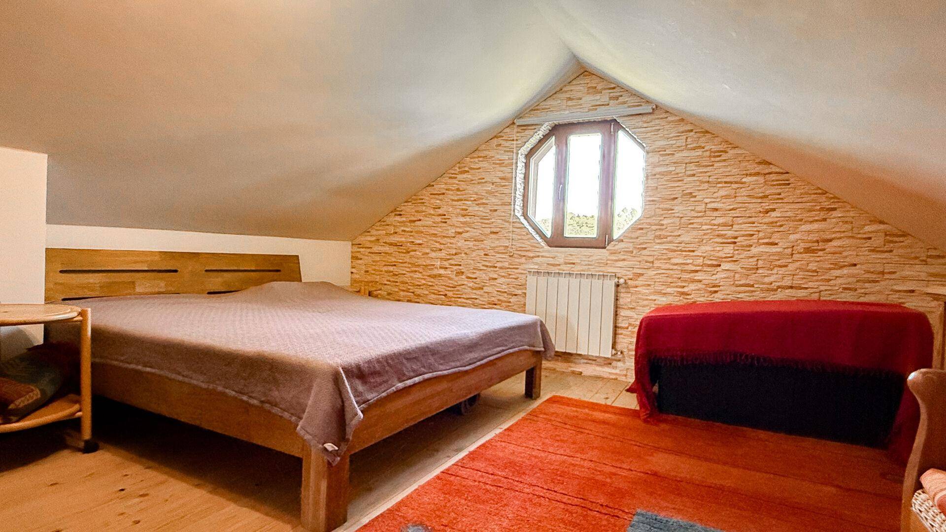 Gemütliches Dachgeschoss-Schlafzimmer mit Holzbett, schräger Decke und einem besonderen Fenster.