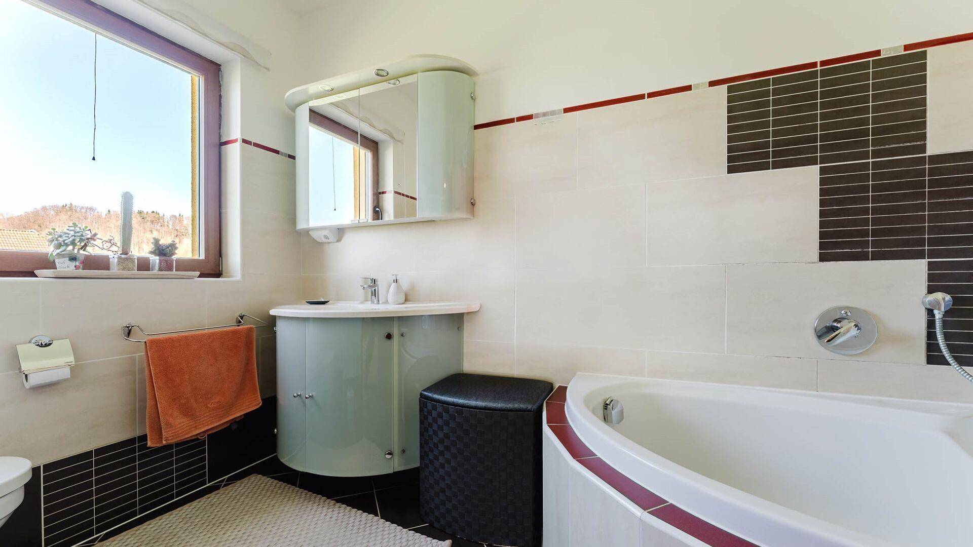 Badezimmer mit Eckbadewanne, Einzelwaschbecken, Fenster und dekorativen Fliesen.