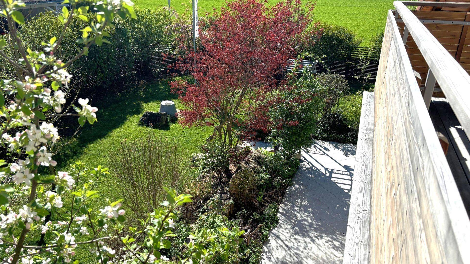 Gepflegter Gartenbereich mit Rasenfläche, blühenden Bäumen und Sträuchern von oben betrachtet.