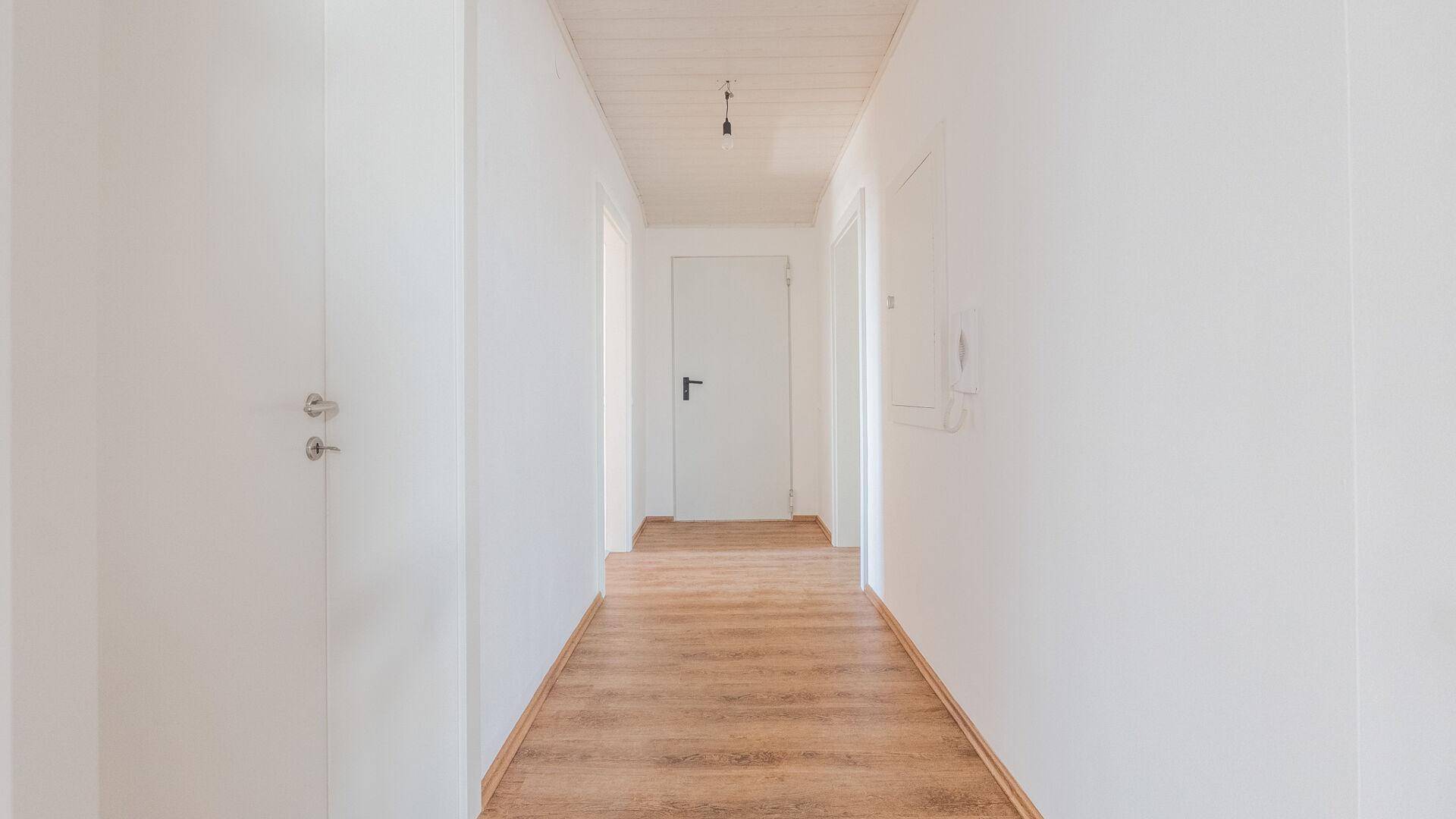 Langer, heller Flur mit Laminatboden und weißen Wänden, der zu weiteren Räumen führt.