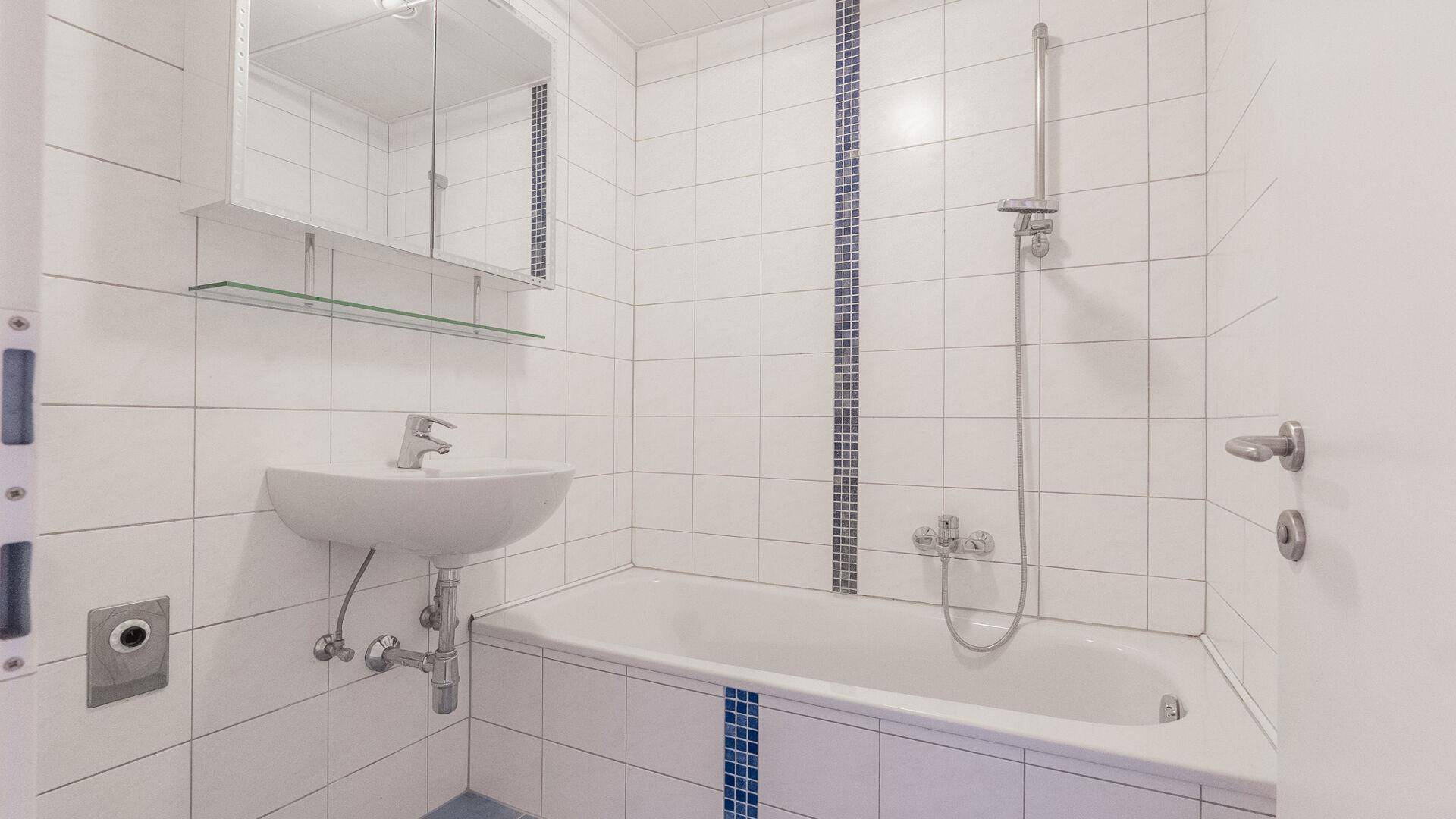 Badezimmer mit Badewanne, Waschbecken, Spiegelschrank und weißen Fliesen.